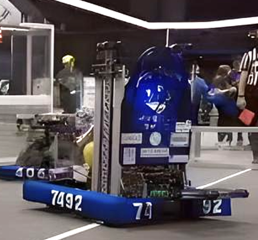 A robotics team robot at a competition, with a blue body and various numbers and logos, surrounded by people and a security guard in an indoor setting.