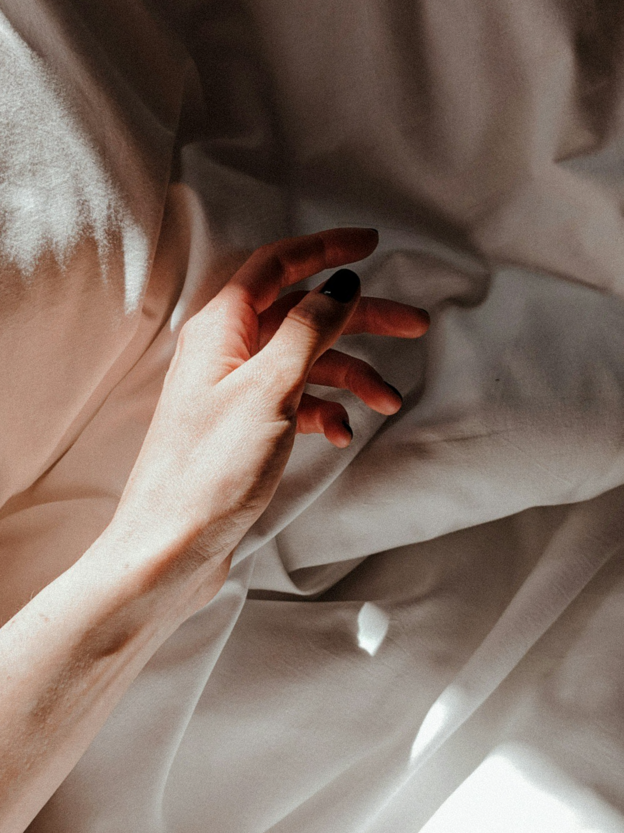 Close-up of a hand with black nail polish resting on soft, light-colored fabric.
