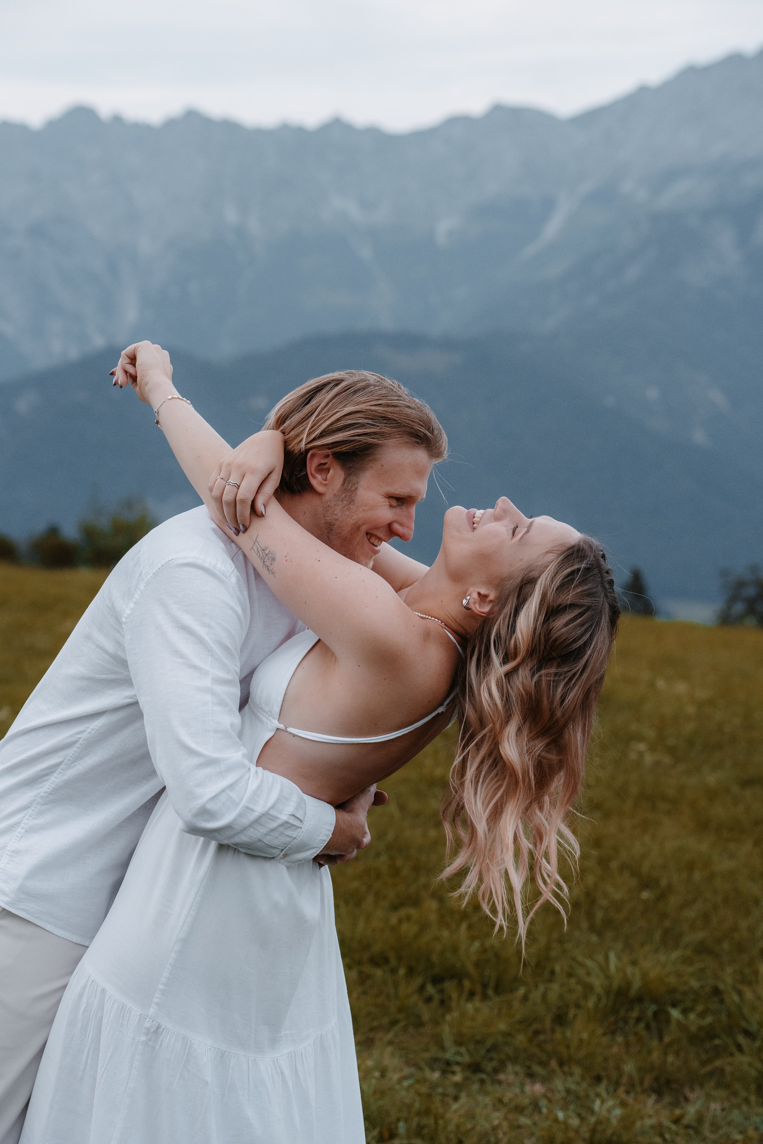 Ein Paar tanzt im Freien vor einer Bergkulisse, lächelt und schaut sich verliebt an.