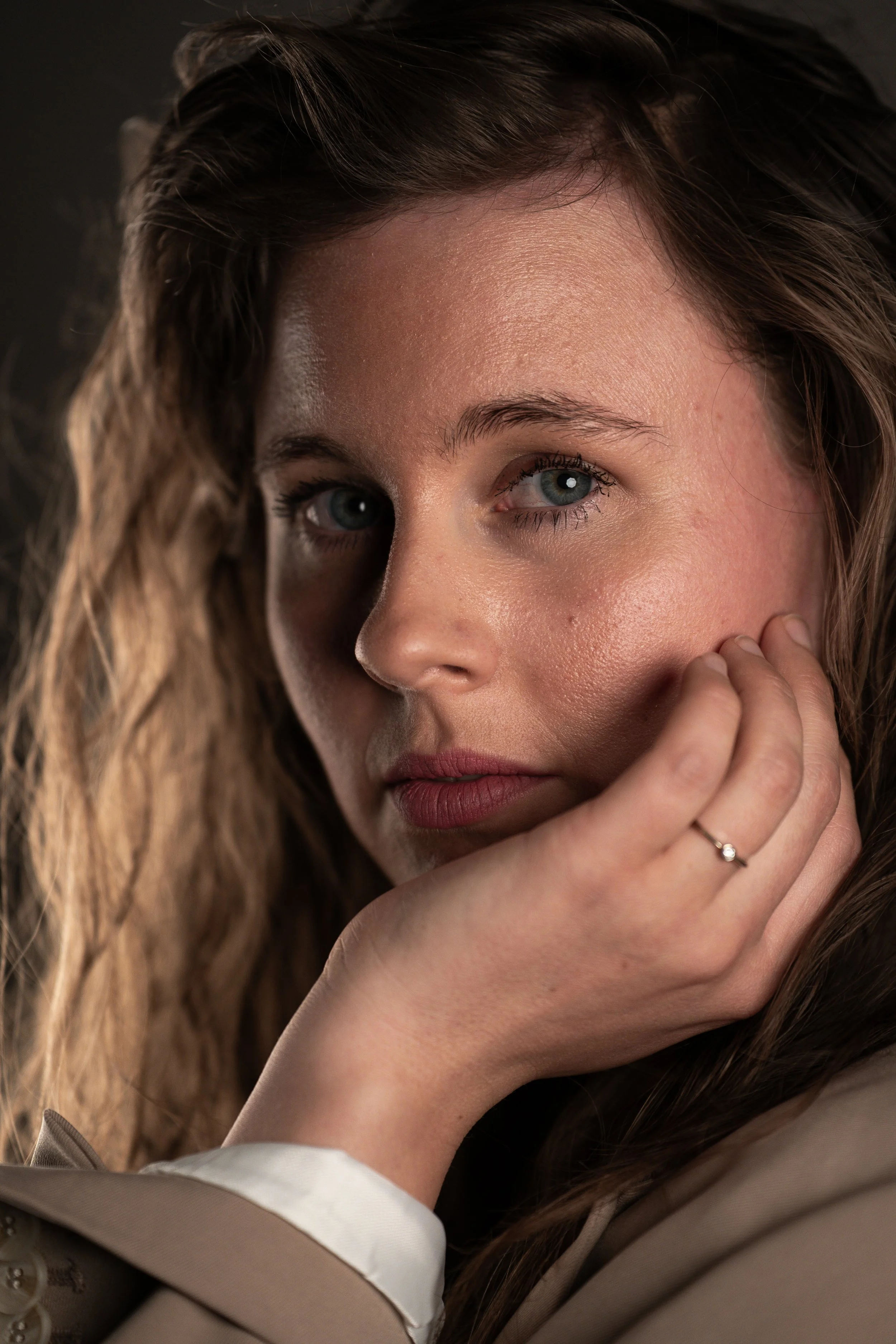 Nahaufnahme eines Mädchens mit blonden, gewellten Haaren, blauen Augen und rotem Lippenstift, das die Hand an das Gesicht legt.