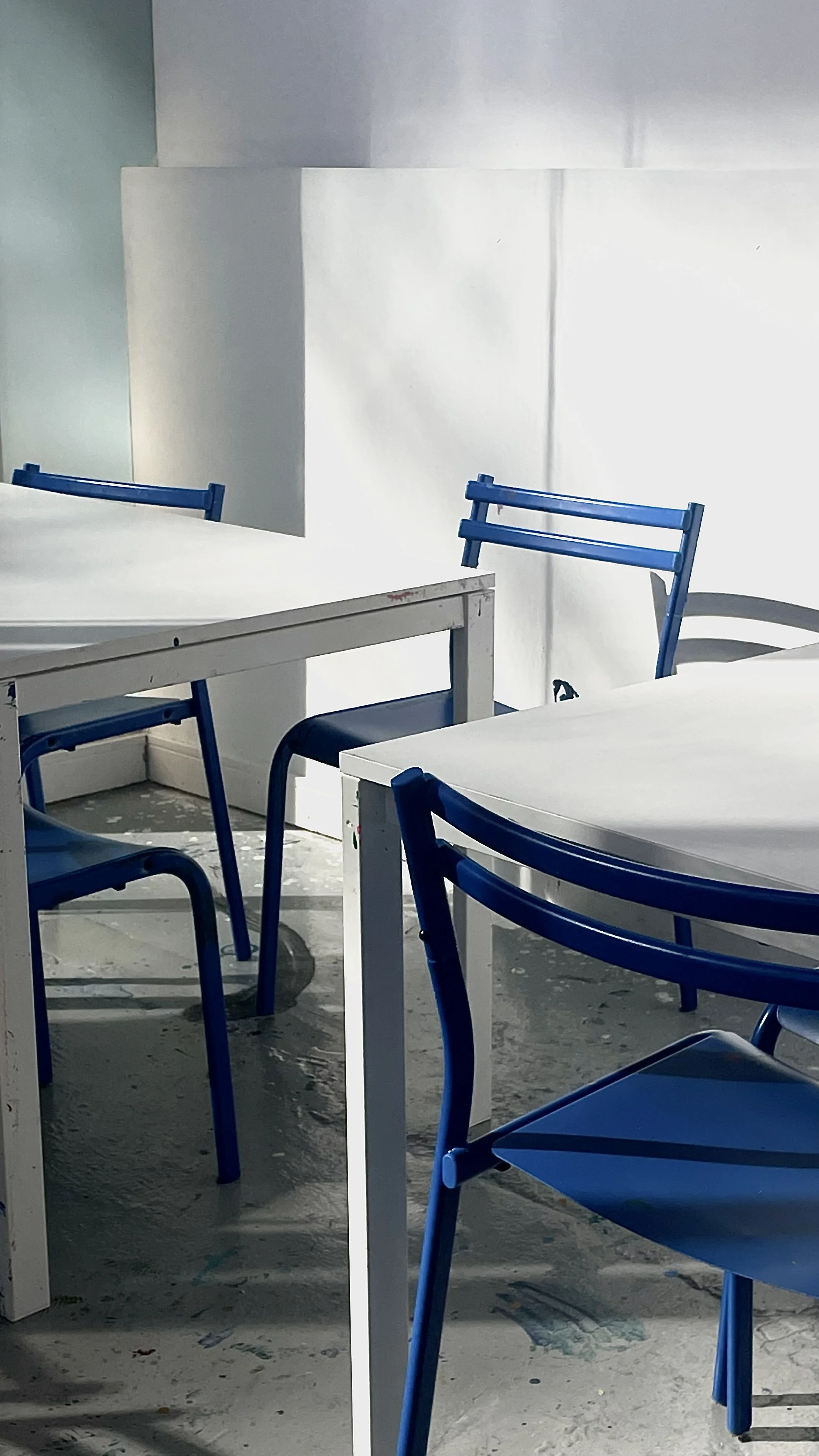 Empty white tables and blue chairs in a brightly lit room with white walls.