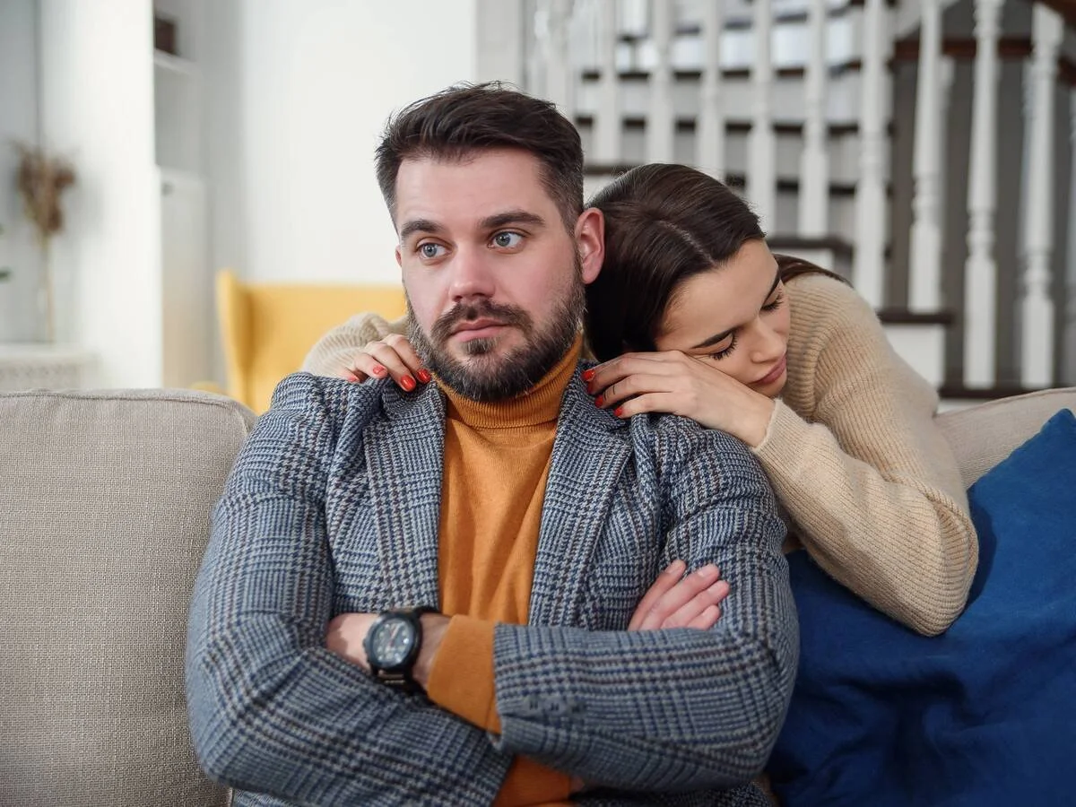 Woman reaching toward her partner after a fight while he looks withdrawn and tense, showing pursue–withdraw pattern.