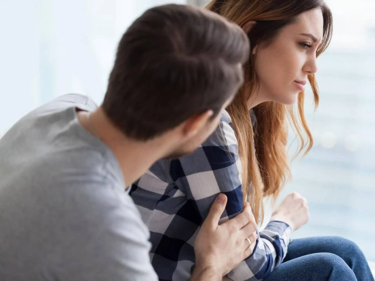 Couple sitting together looking disconnected, partner reaching out while the other turns away—illustrating communication breakdown in marriage.