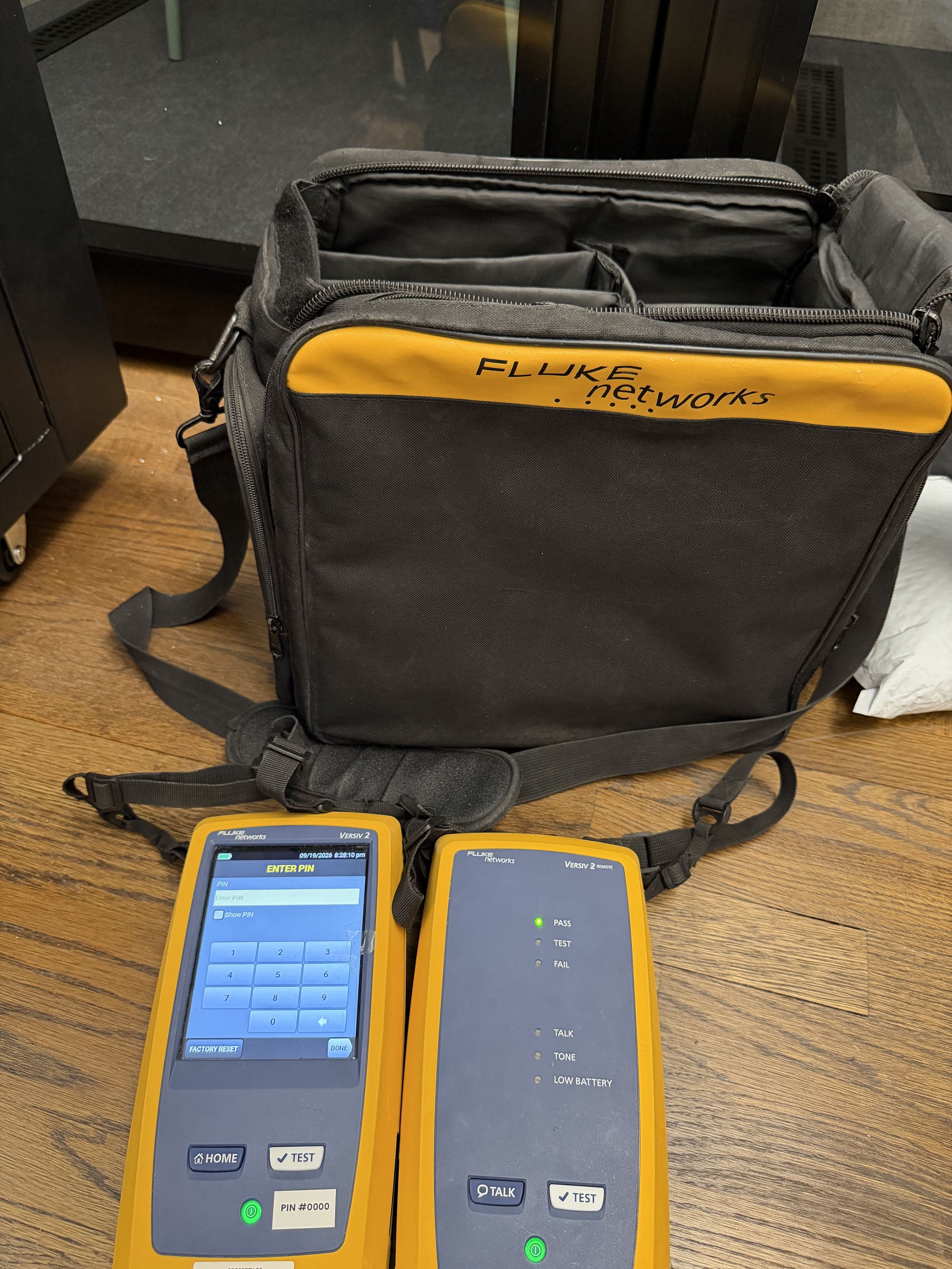 Cable certification test set with the main touchscreen unit and remote unit beside its equipment bag.