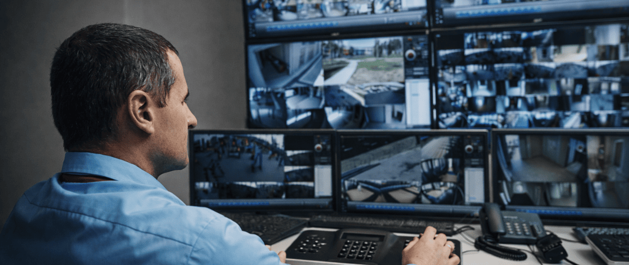 Security operations center technician monitoring multiple live CCTV feeds across commercial and residential properties, demonstrating centralized video surveillance and real-time incident response for New York City buildings.