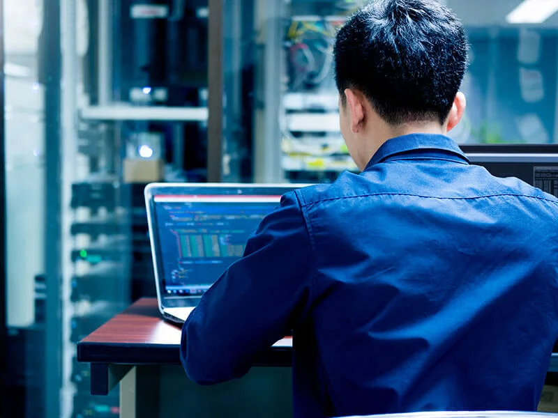 IT specialist monitoring network security systems on laptop in data center.