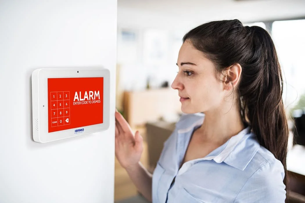 Woman interacting with a wall-mounted alarm system keypad displaying an active security alert.