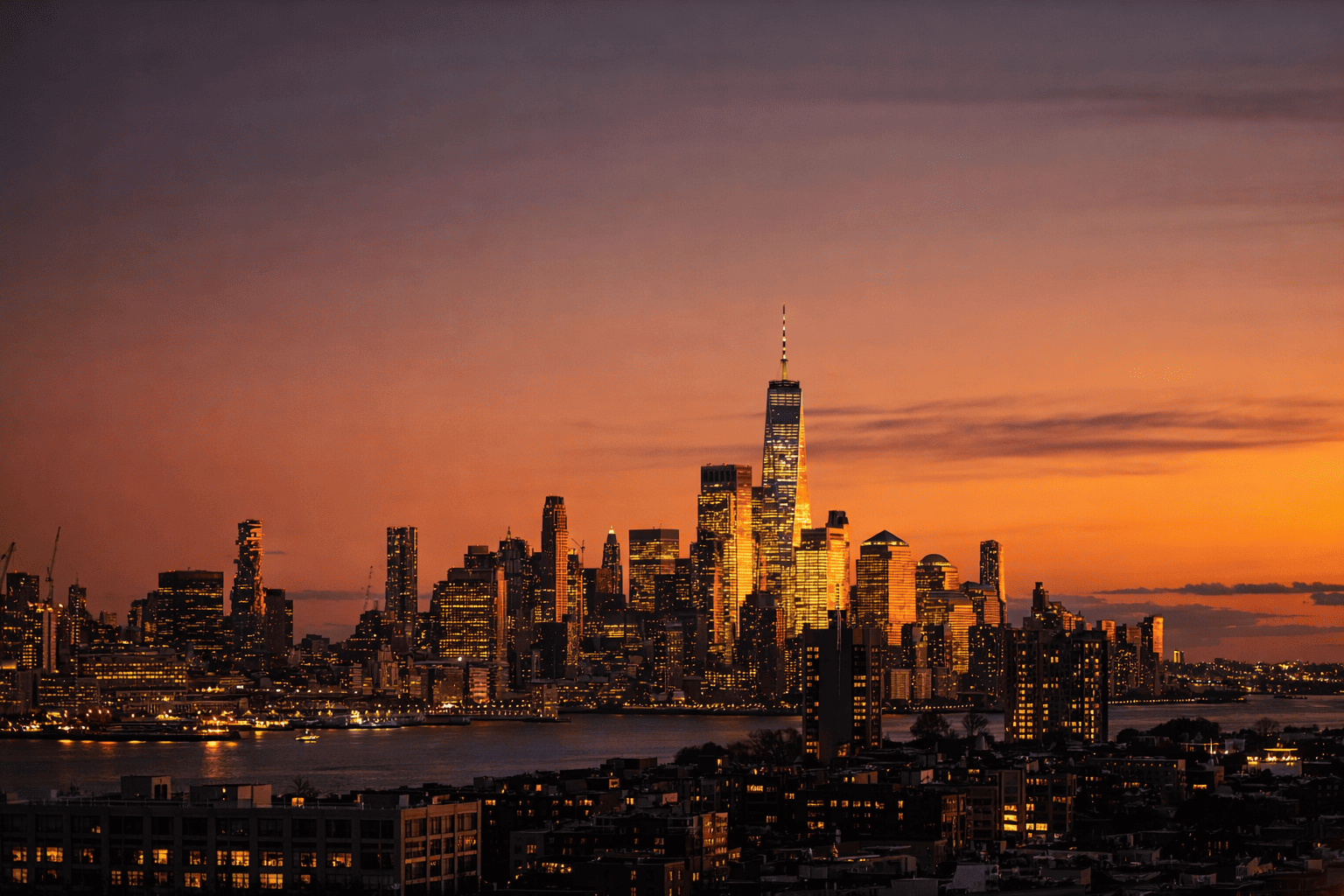 New York City skyline at sunset with illuminated skyscrapers and waterfront views.