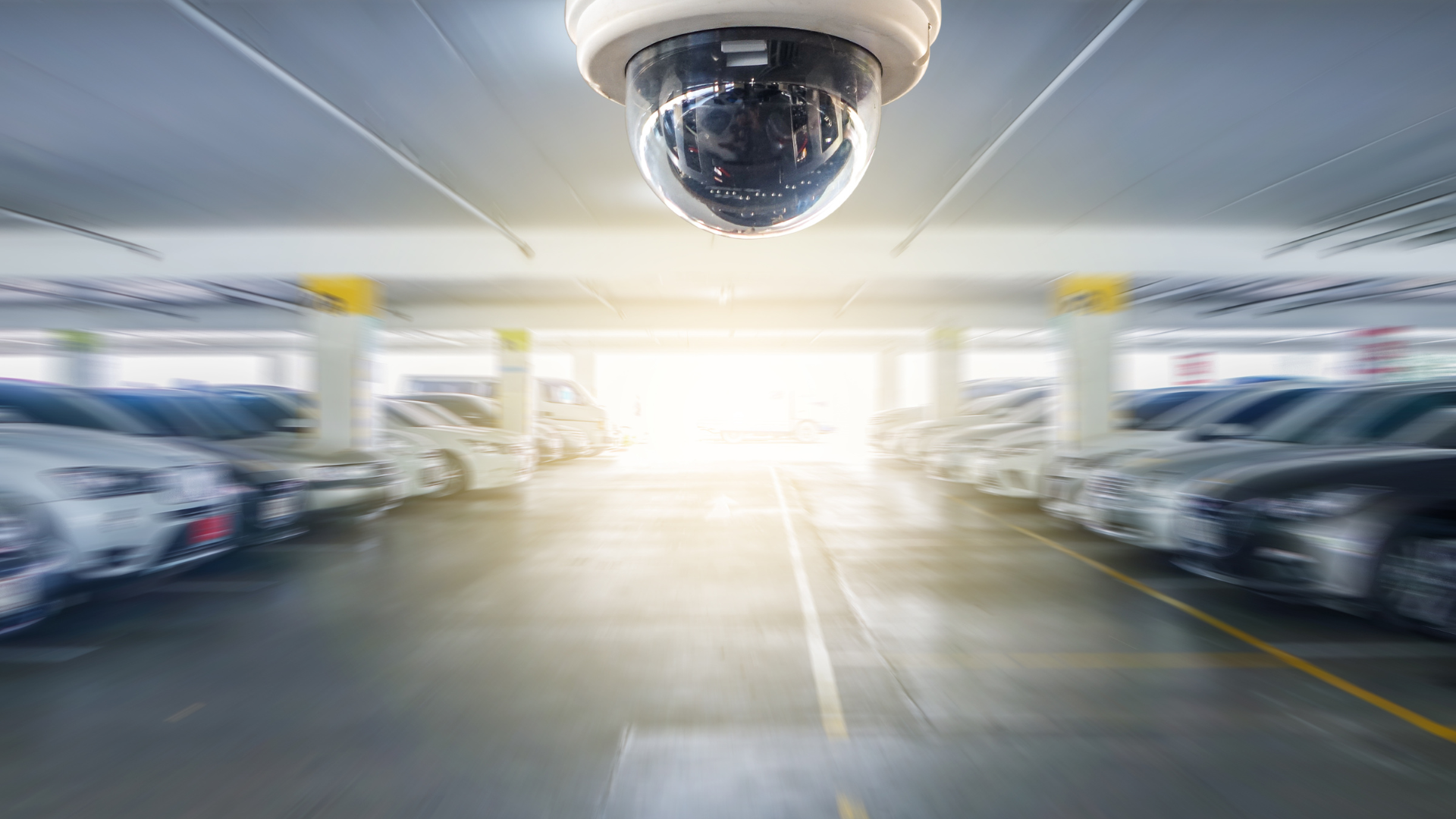 Security camera monitoring vehicles and pedestrian activity in a parking facility, representing transportation and parking security systems.