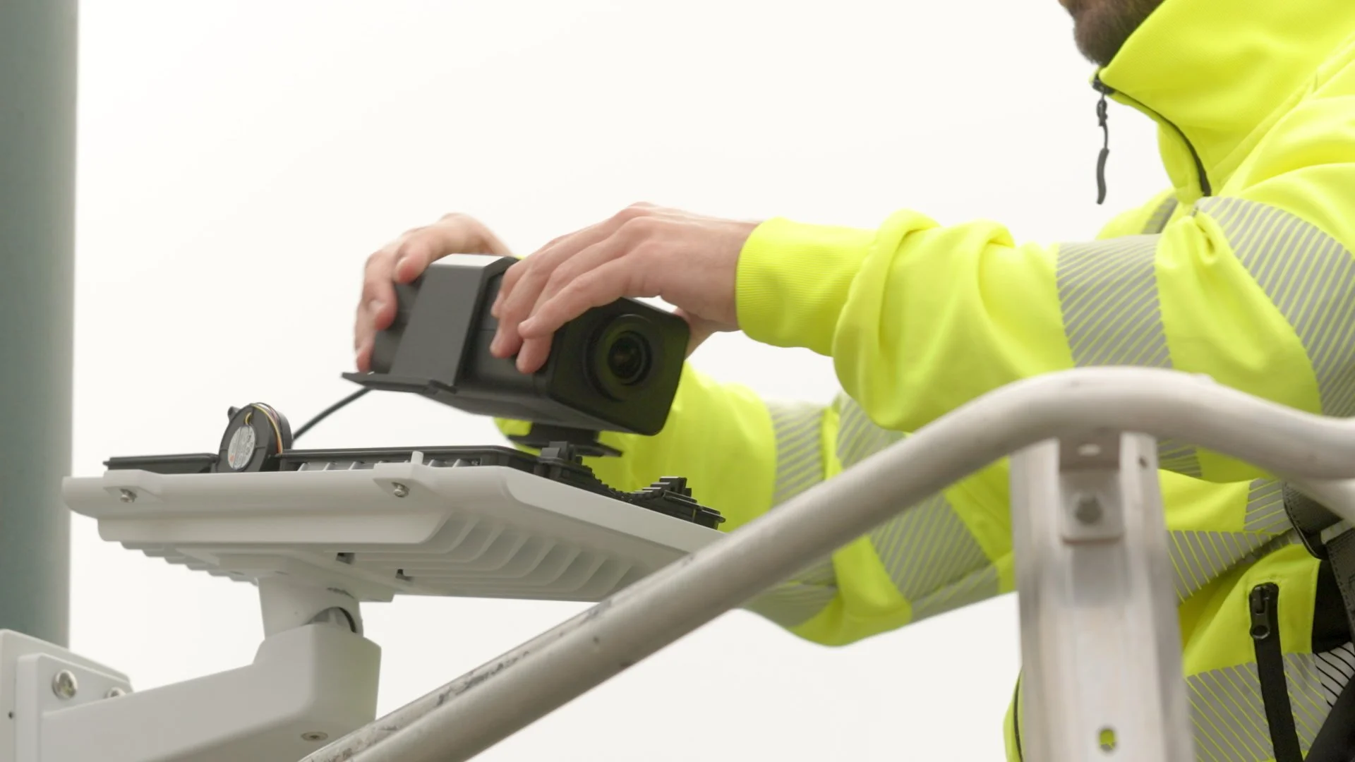 Security Technician in a reflective neon yellow jacket opening a security camera, performing security assessment and maintenance