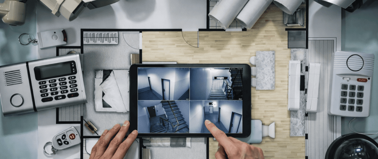 Remote security monitoring setup showing live camera feeds reviewed on a tablet alongside alarm keypad and access control devices during system planning