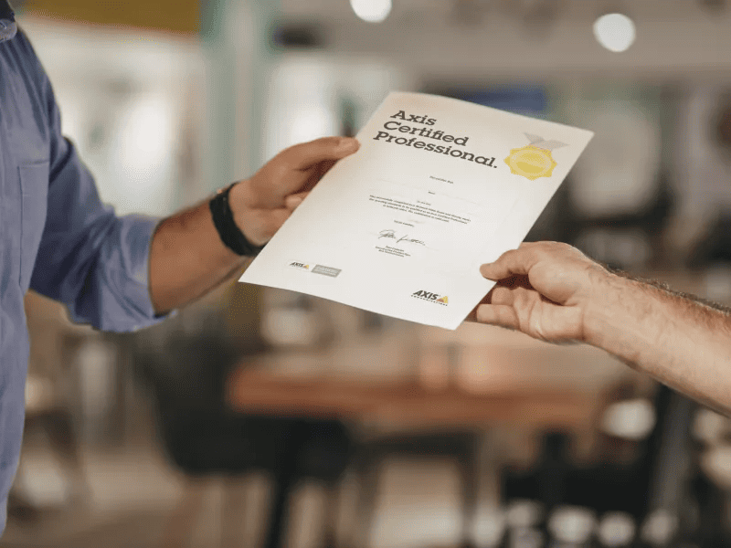 Two professionals holding an Axis Certified Professional certificate in a commercial office setting.