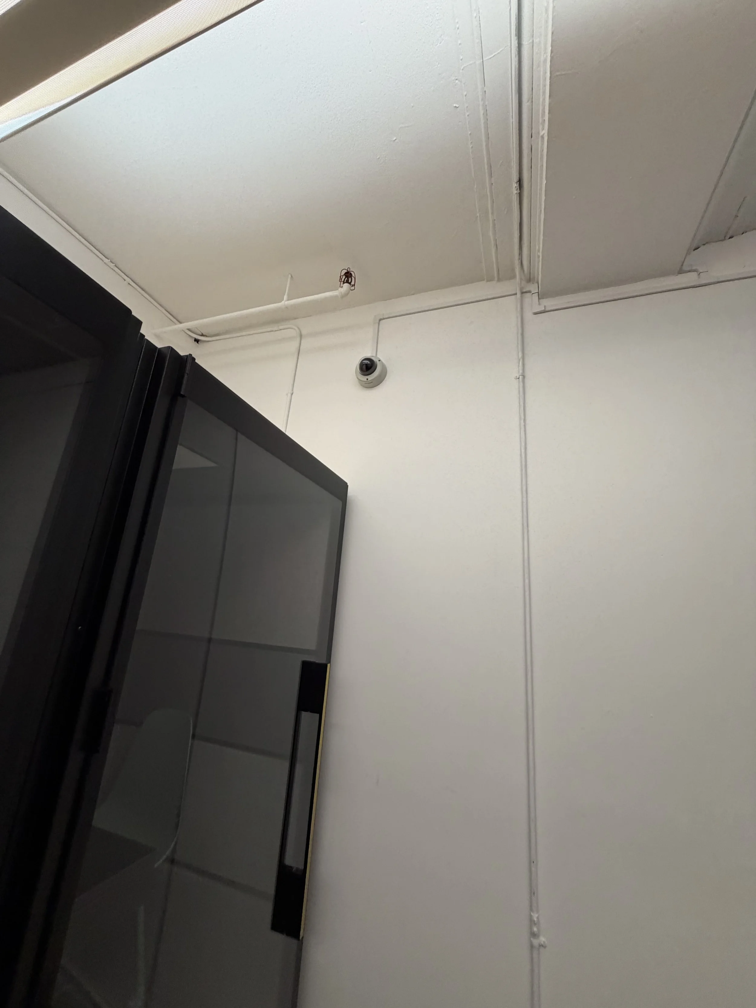 Security camera and white surface raceway on an office wall beside conference pods