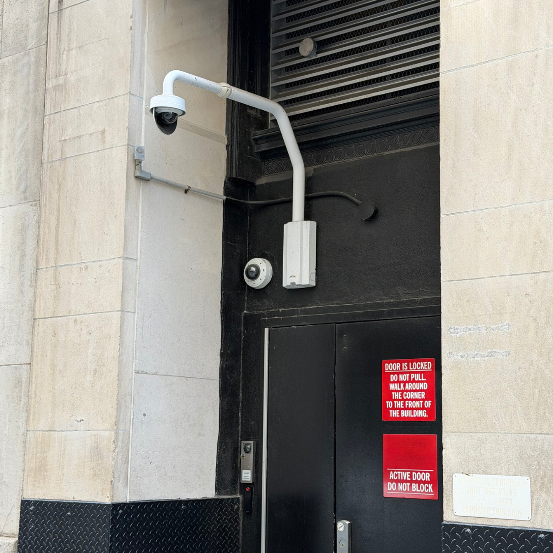 Security cameras installed above a commercial building service entrance to monitor access and reduce blind spots in Manhattan, NYC.