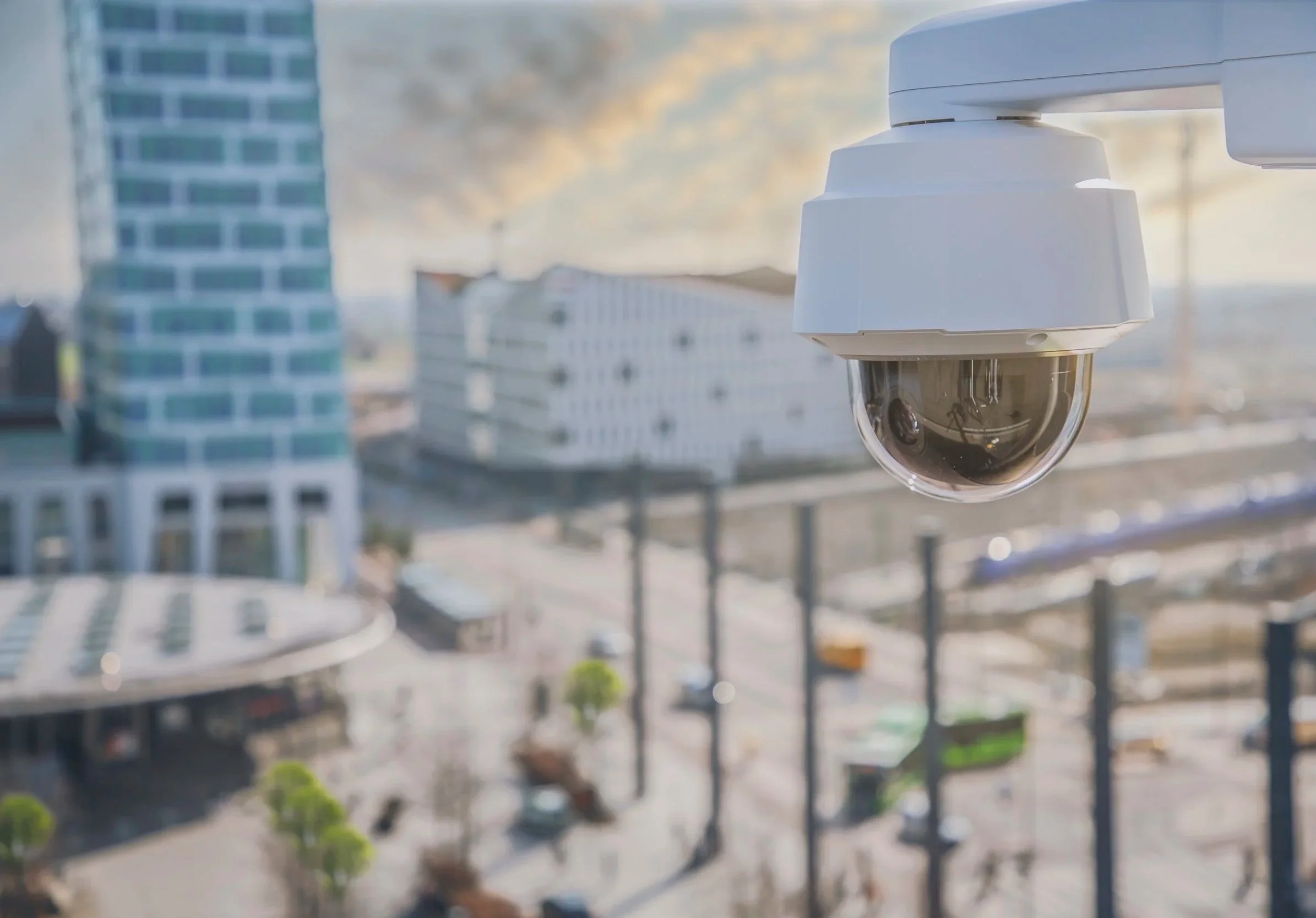 Security camera mounted on a building overlooking a city street with tall buildings and traffic.