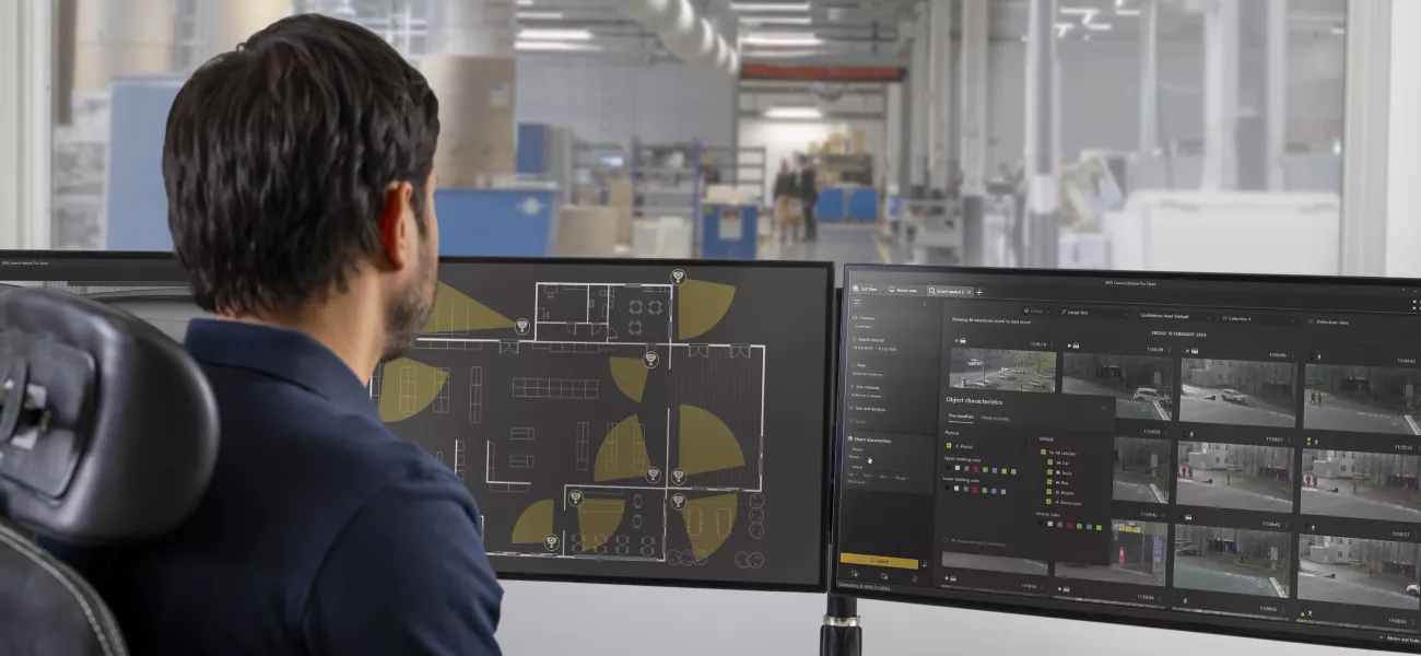 Security operator monitoring Axis enterprise video surveillance system across multiple displays in a control room.