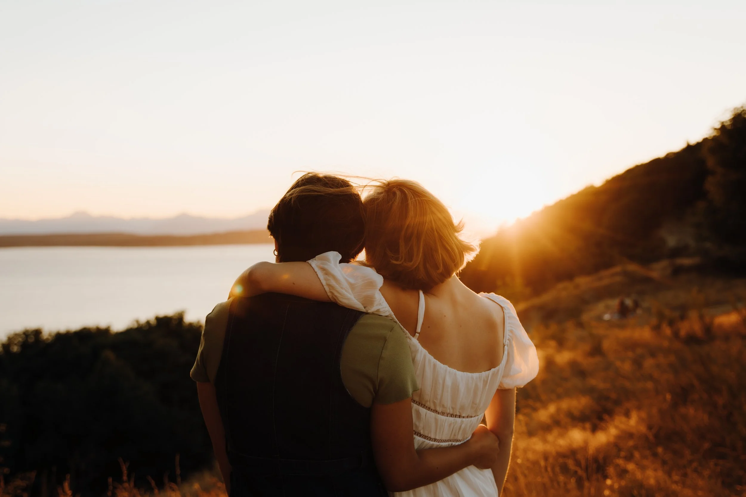 A couple embracing while watching a sunset over a lake and hills.