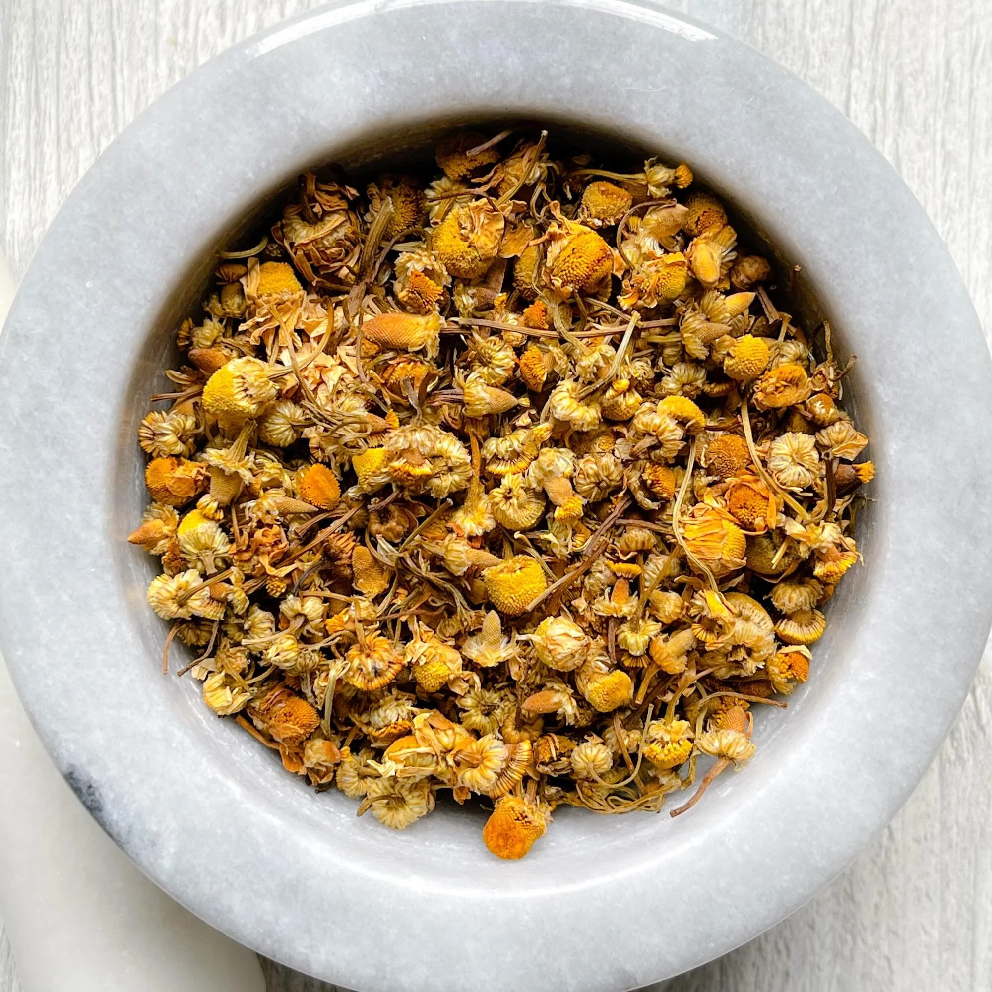 organic-german-chamomile-tea.jpeg: loose organic German chamomile tea in a mortar