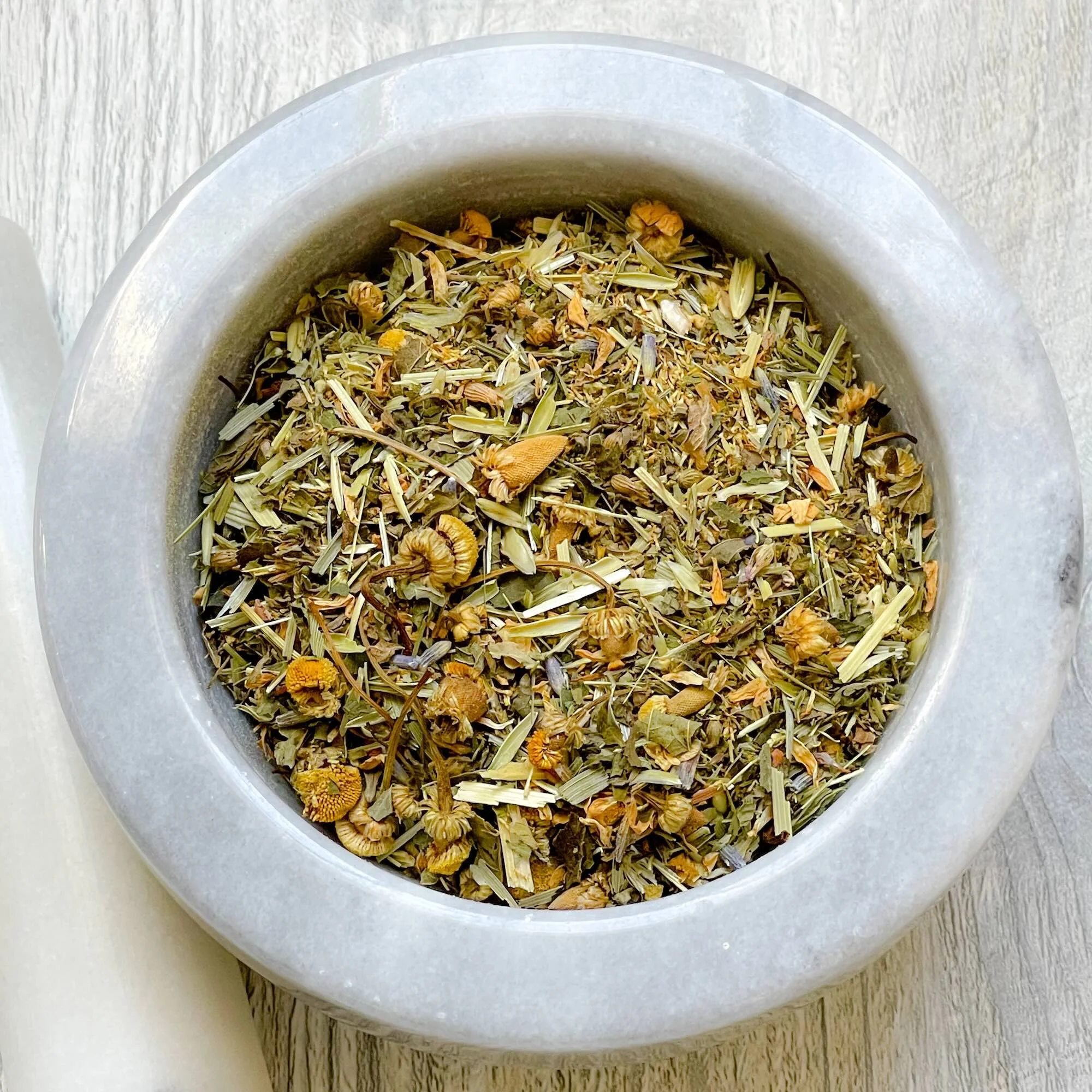 chamomile-comfort-herbal-tea-blend-loose.jpeg: loose chamomile comfort herbal tea blend in a mortar