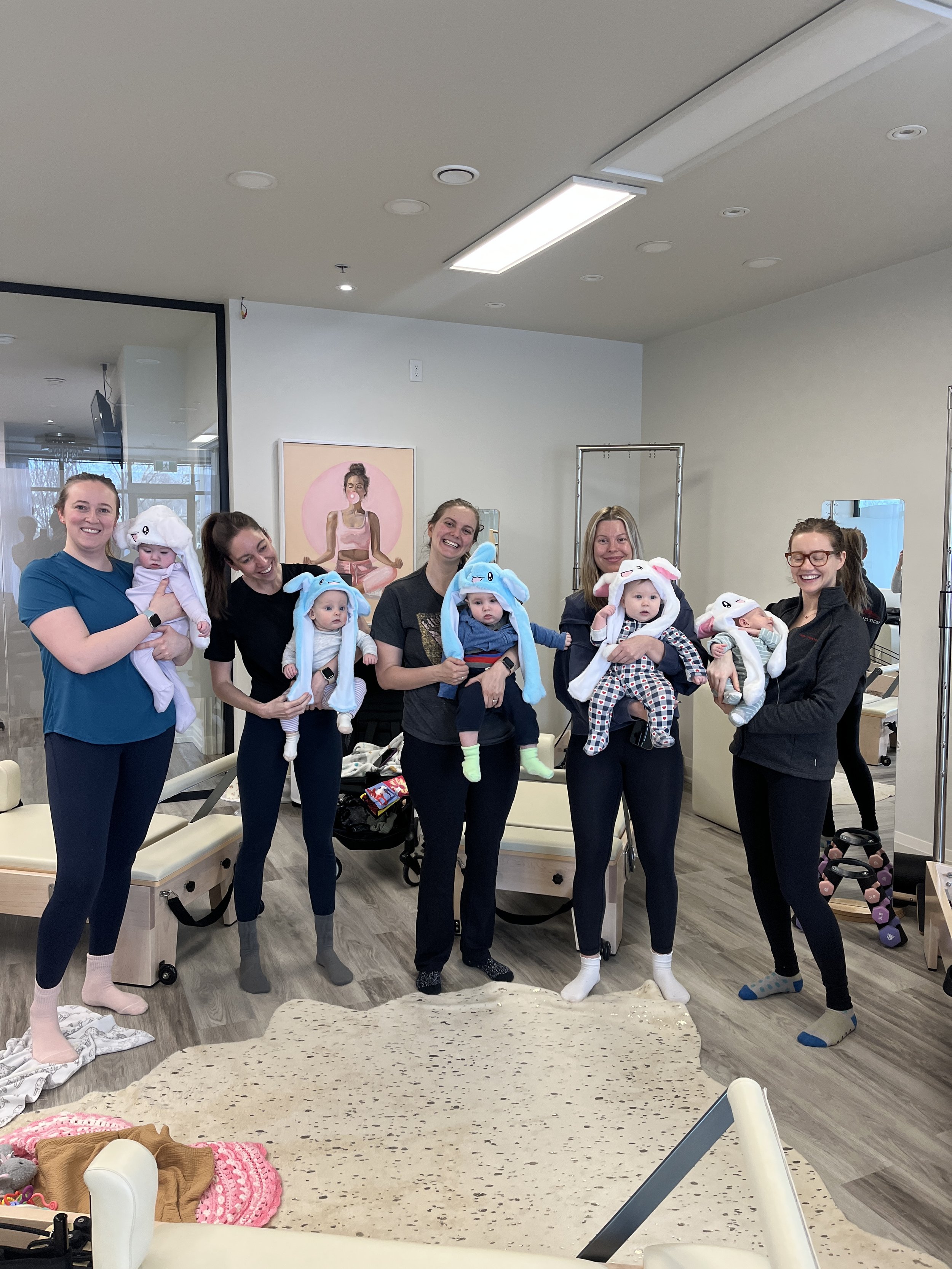 Postpartum moms participating in a Pilates reformer class with their babies at Pilates on Plains studio in Burlington.