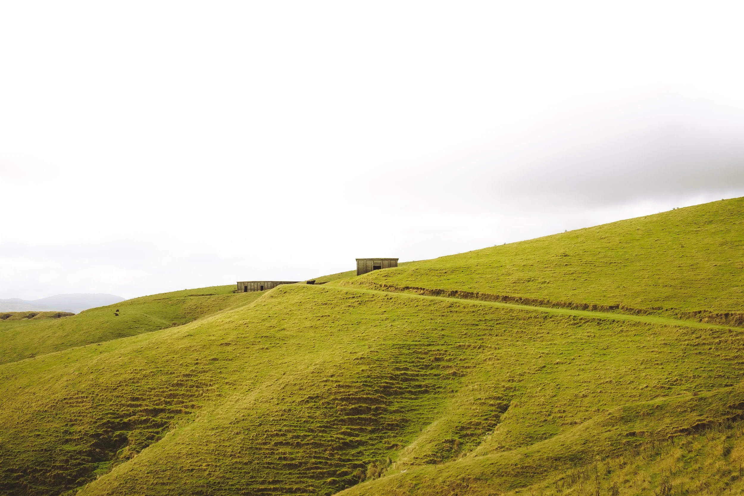 Green hilly landscape with a few small structures on a cloudy day.