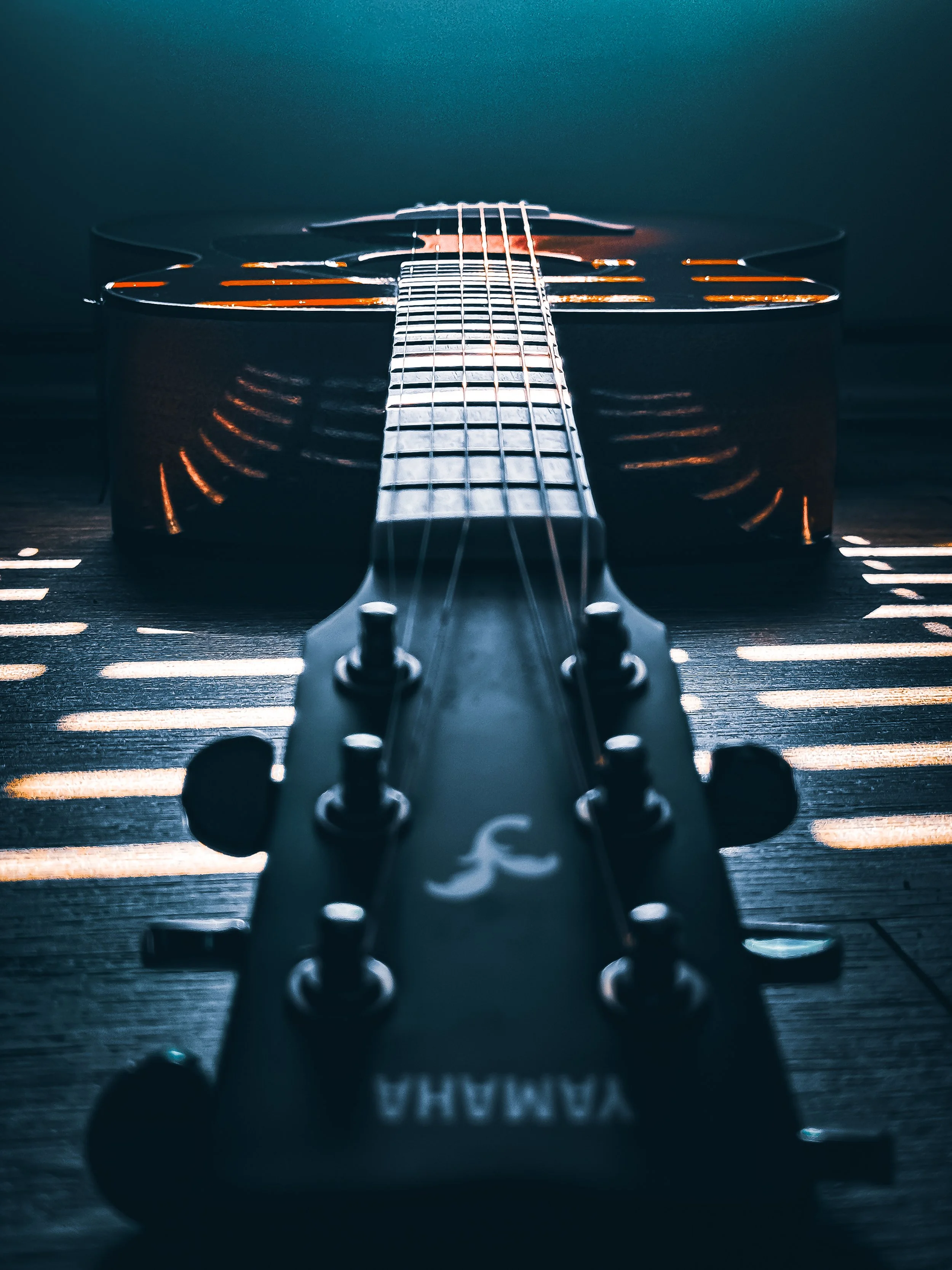 Close-up of a black Yamaha acoustic guitar viewed from the headstock to the body, with strings and tuning pegs visible, lying on a dark wooden surface.