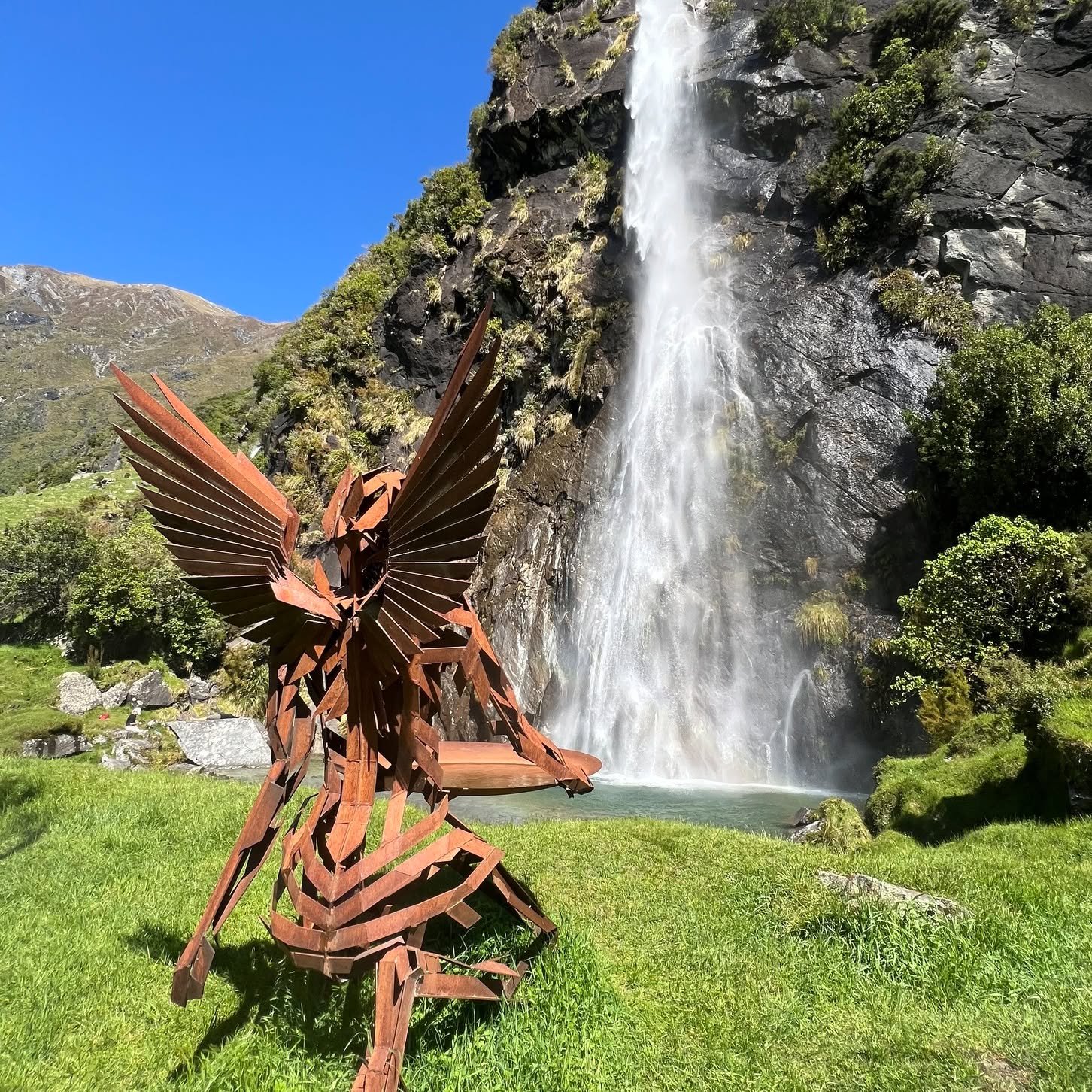 'Iris' kneeling at Wishbone Falls. This stunning statue sits on the edge of Wishbone Falls in the Matukituki valley. Inspired by the Greek Goddess of the rainbow, she is there to catch the prisms from the waterfall 🌈. This image was captured by our 