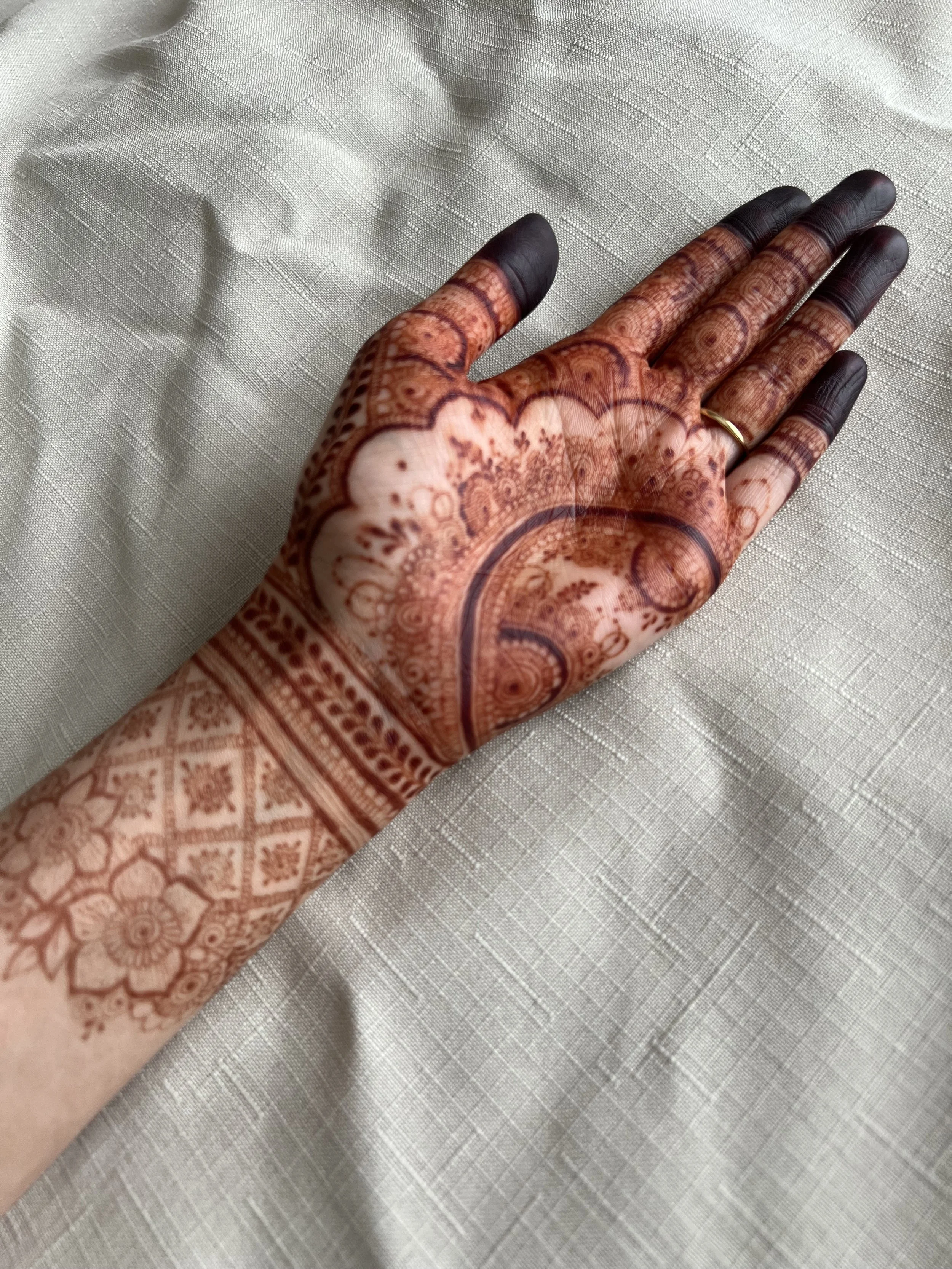 Close-up of a hand with intricate henna design showing dark maroon red and black henna stain resting on a light-colored fabric surface.