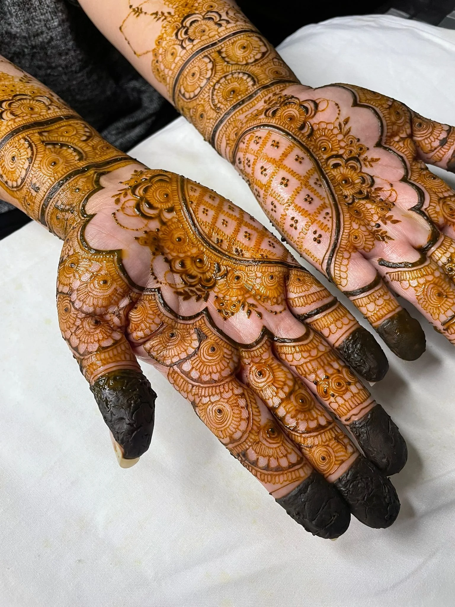 Close-up of hands decorated with intricate henna tattoo designs in gold and black, with blackened fingertips.