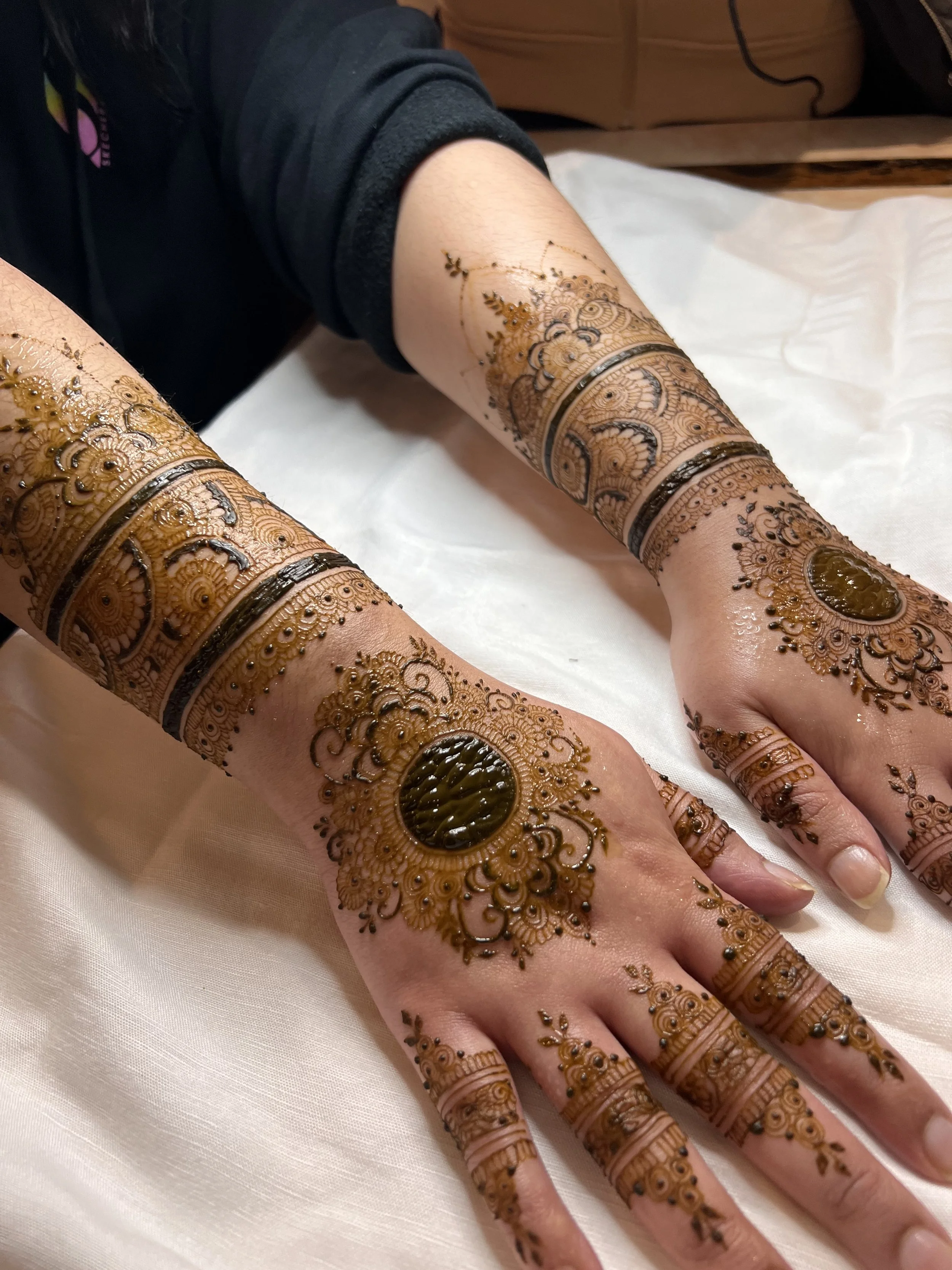 Close-up of hands with intricate bridal henna (mehndi) designs, including floral and geometric patterns, on fingers, palms, and wrists.