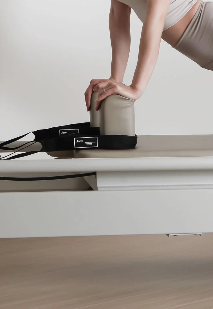 Person performing a plank exercise on a padded bolster with their hands on a padded surface, positioned on a low table or bed.
