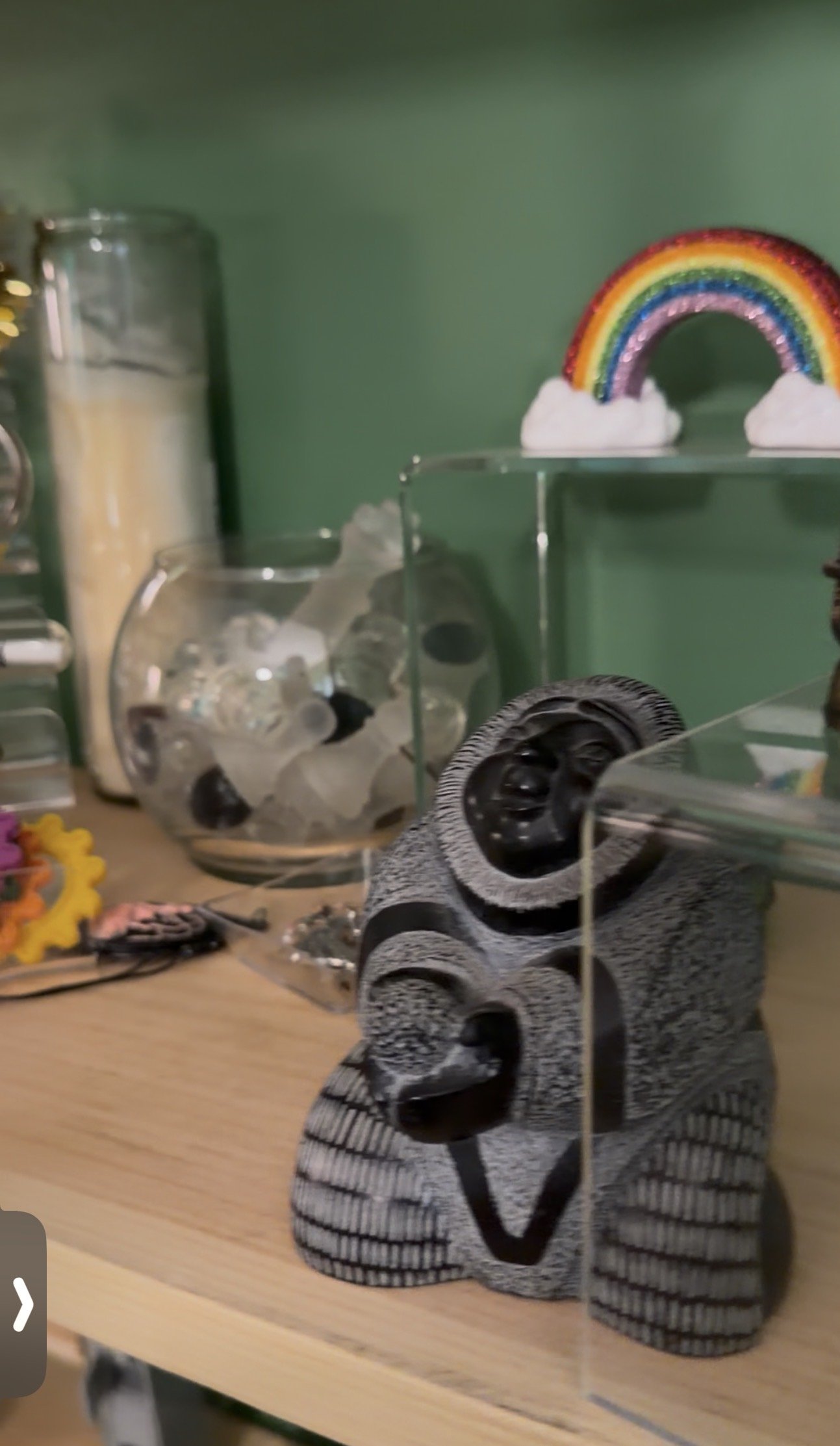 Therapy room shelf with sensory and symbolic objects including crystals, a rainbow, fidget tools, and a meditative figurine against deep green walls and warm calming light.