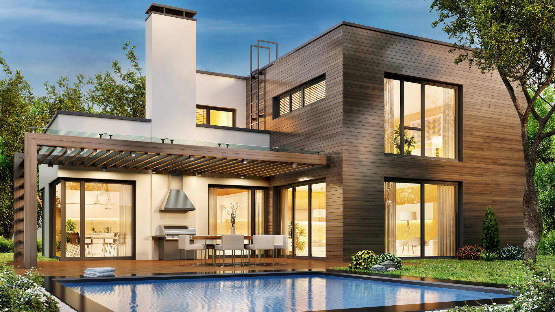 Modern two-story house with large glass windows, an outdoor patio with a dining table and chairs, a pool in the yard, and lush greenery surrounding the property at sunset.