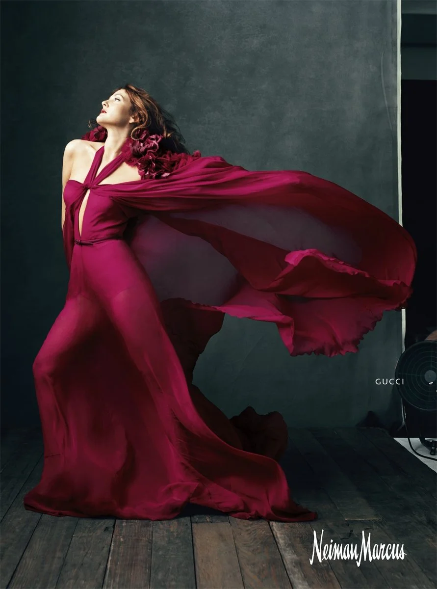 A woman in a flowing red dress strikes a pose against a dark background, with a Gucci logo and the name Neiman Marcus visible in the corner.