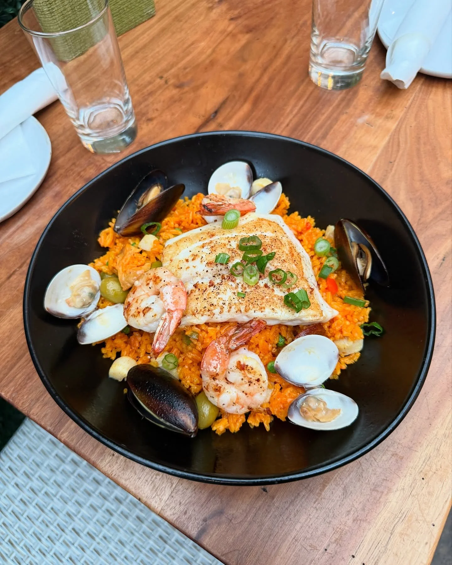 Seafood paella with shrimp, mussels, clams, and a grilled fish fillet garnished with green onions served in a black bowl.