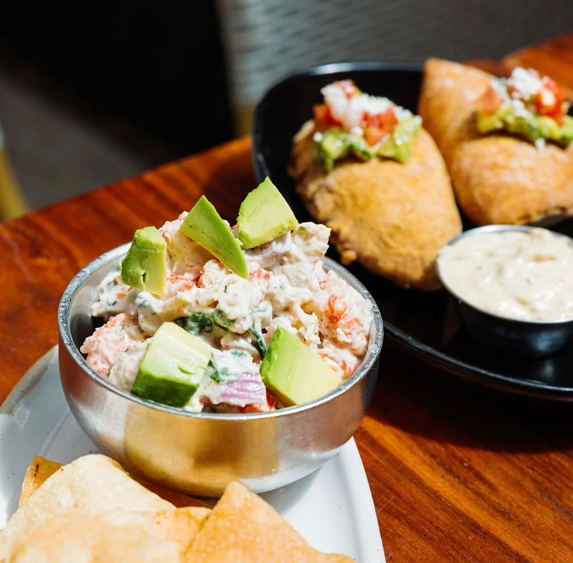 Mexican food with a bowl of avocado salad and two tamales with salsa on a wooden table.