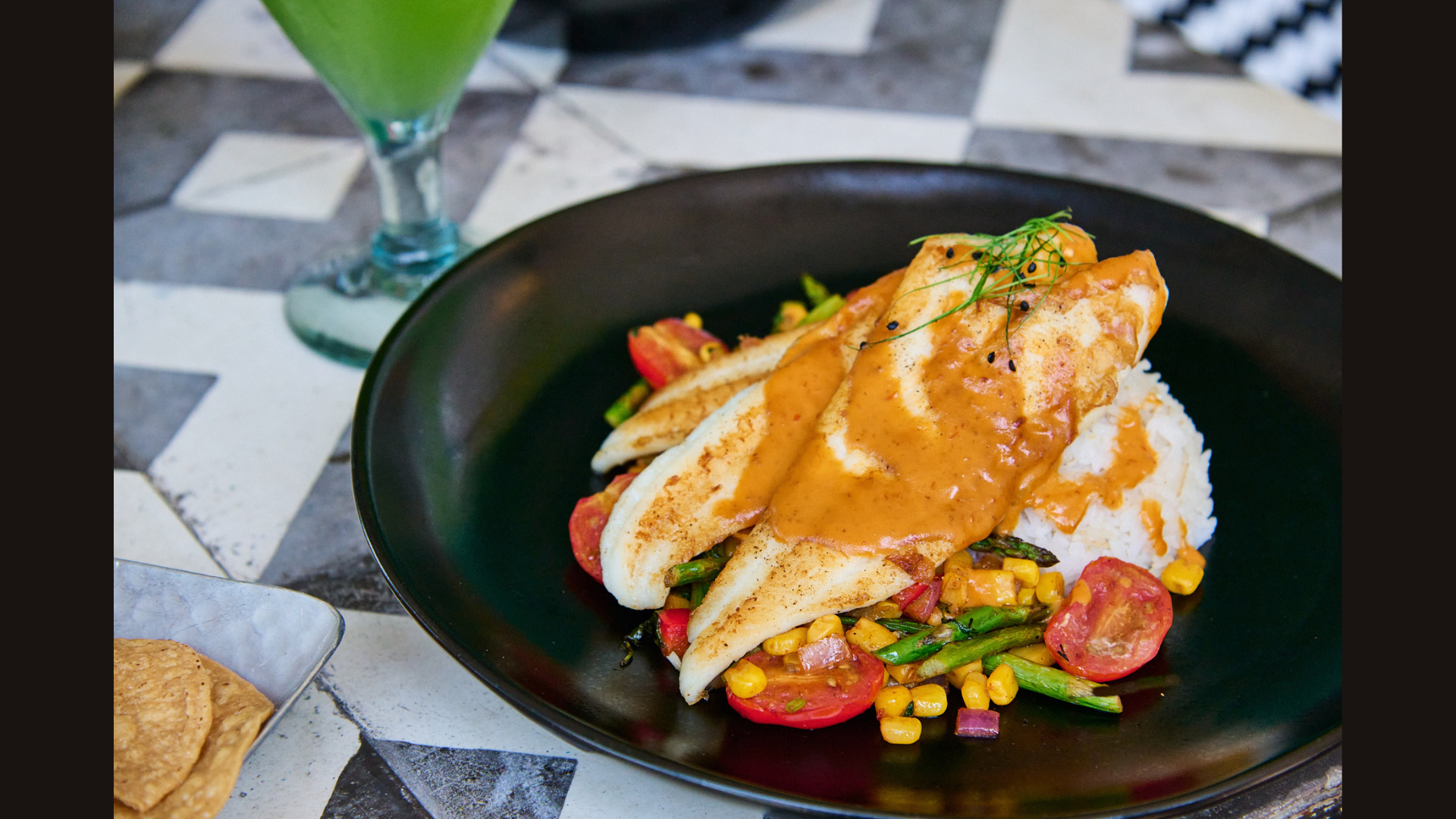 A table outdoors with a glass of water, a bowl of salad with strawberries and cheese, and a plate of cooked meat with vegetables.