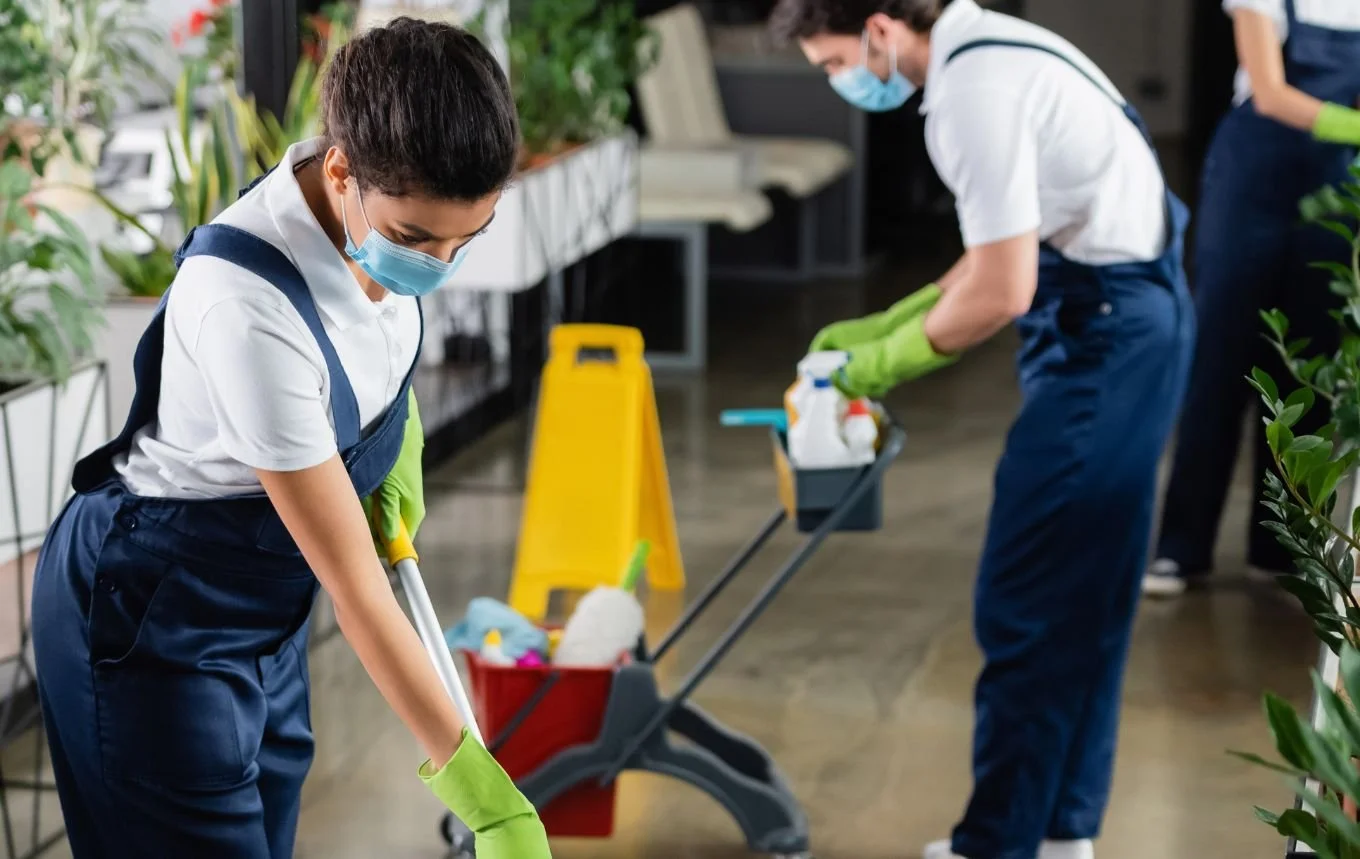 Cleaning service near Perth Australia. Two people wearing masks and gloves cleaning a floor with cleaning supplies in a commercial setting, possibly a grocery store or shop.