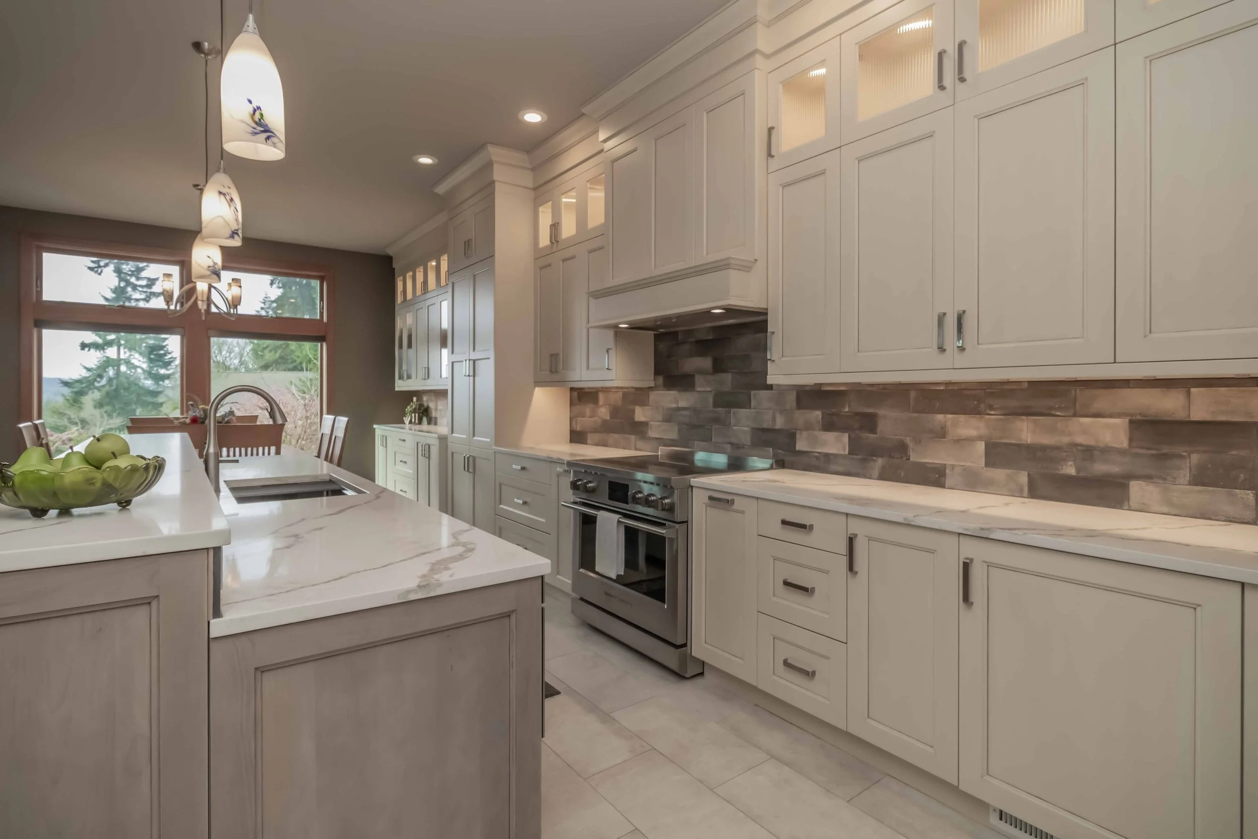 Modern kitchen with white cabinetry, a marble countertop island, gray stone backsplash, stainless steel stove, large windows, and hanging pendant lights.