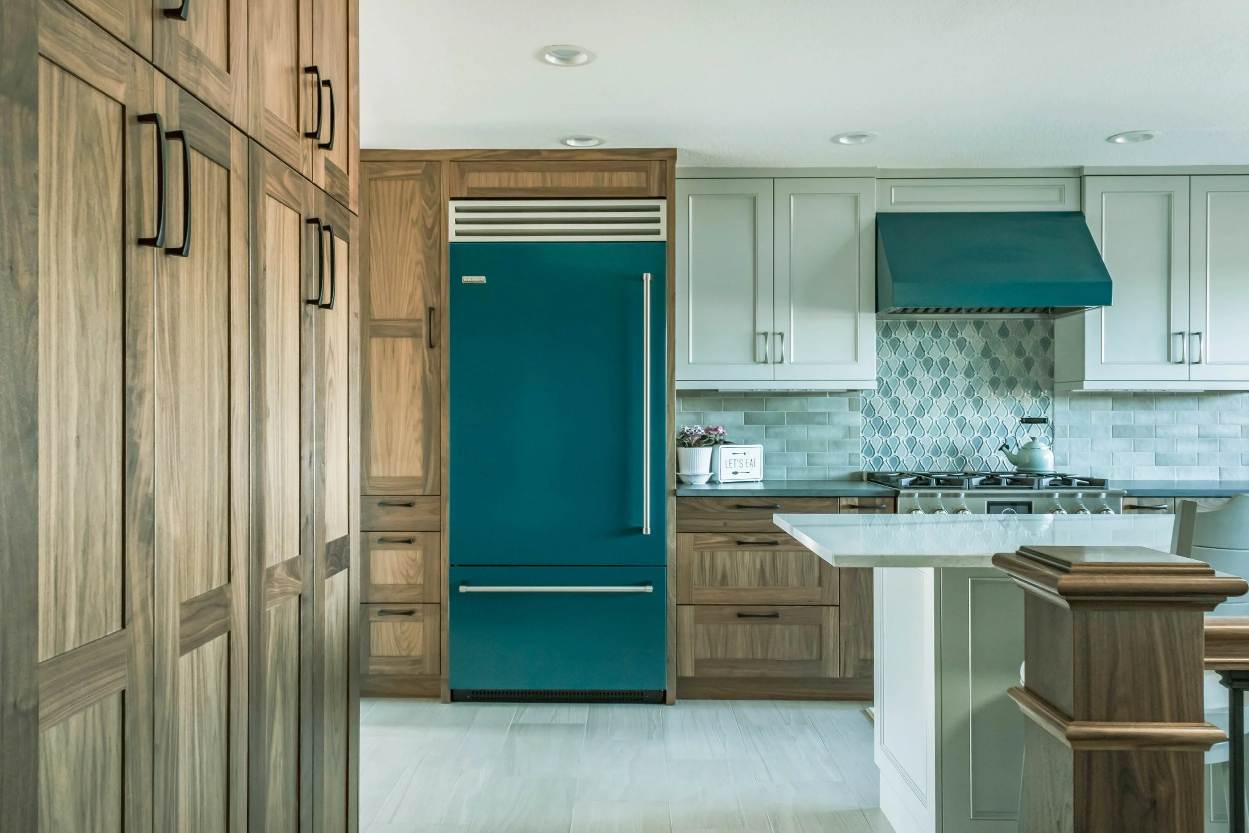 Kitchen with wooden cabinets, a blue refrigerator, white upper cabinets, a blue range hood, a white kitchen island, and a grey tiled backsplash.
