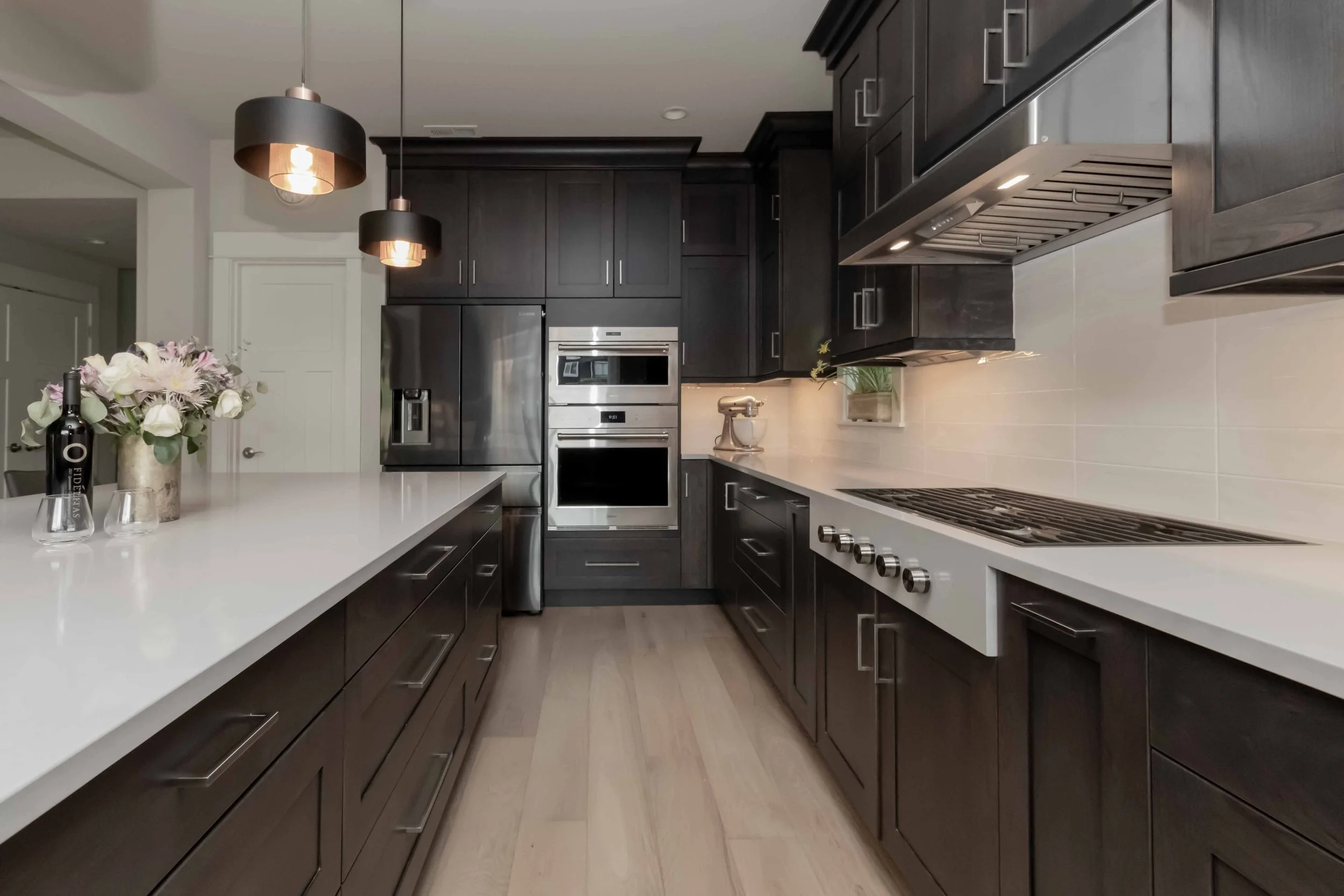 Modern kitchen with dark wood cabinets, white countertops, stainless steel appliances, and pendant lighting.