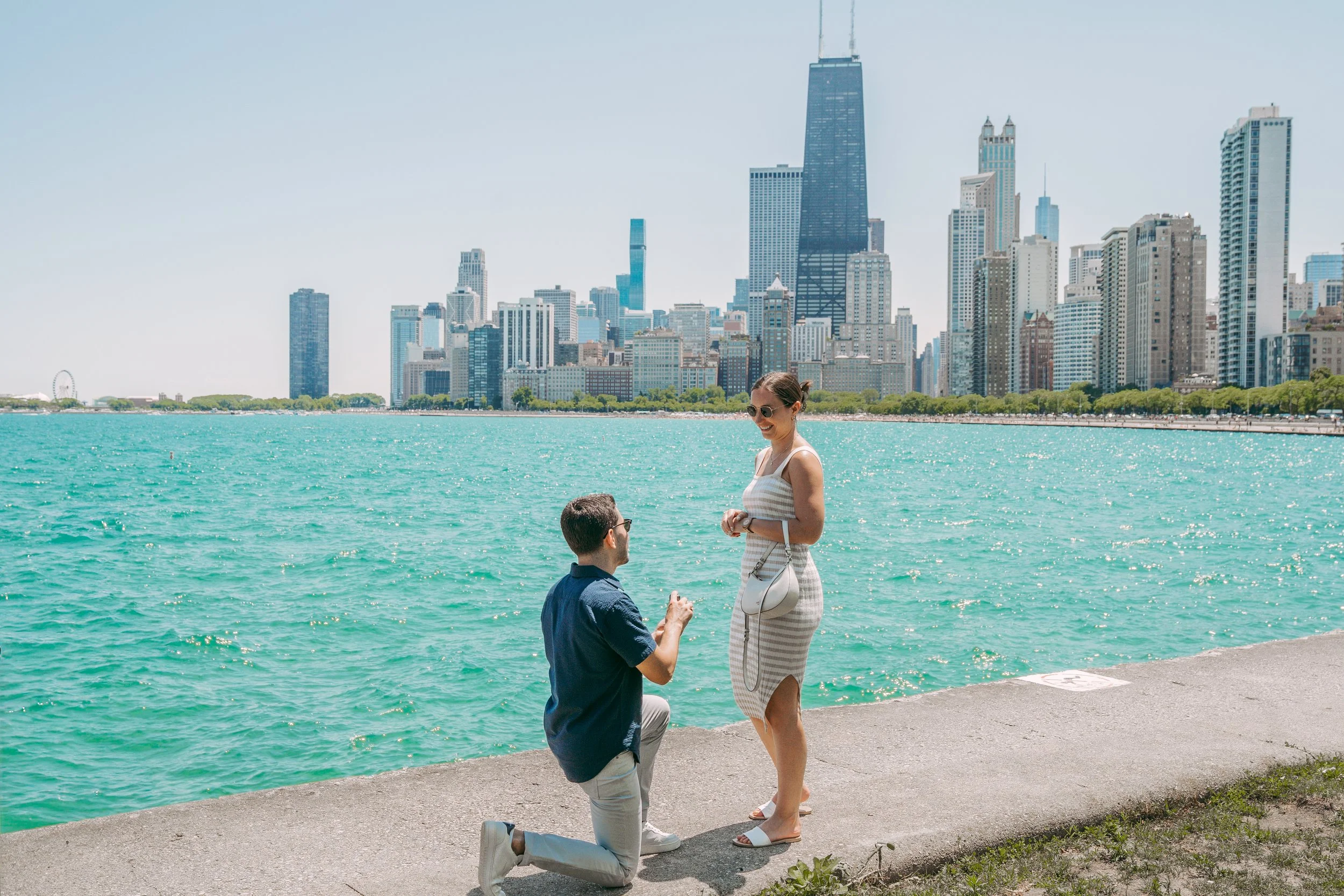 A man proposing to a woman by Lake Michigan with the Chicago skyline in the background.