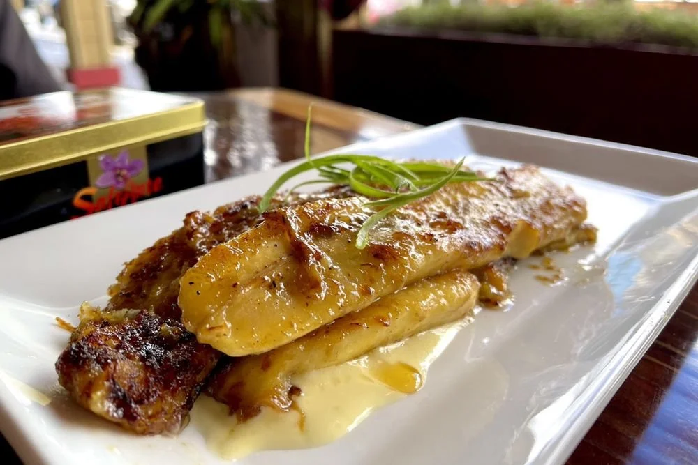A plate of baked fish topped with caramelized onions and garnished with green onions on a white rectangular dish.