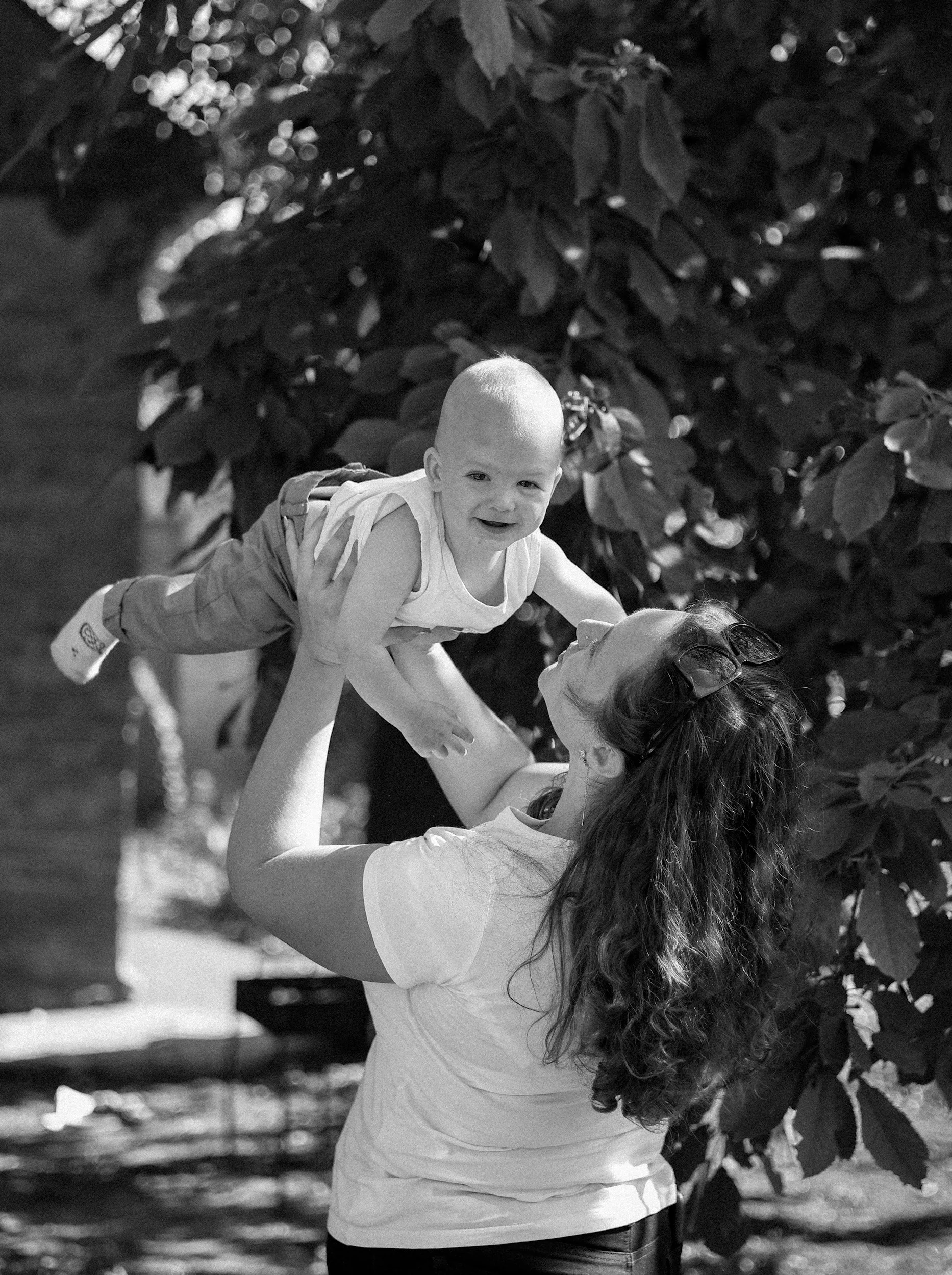 A woman lifting a young child outdoors with trees in the background.