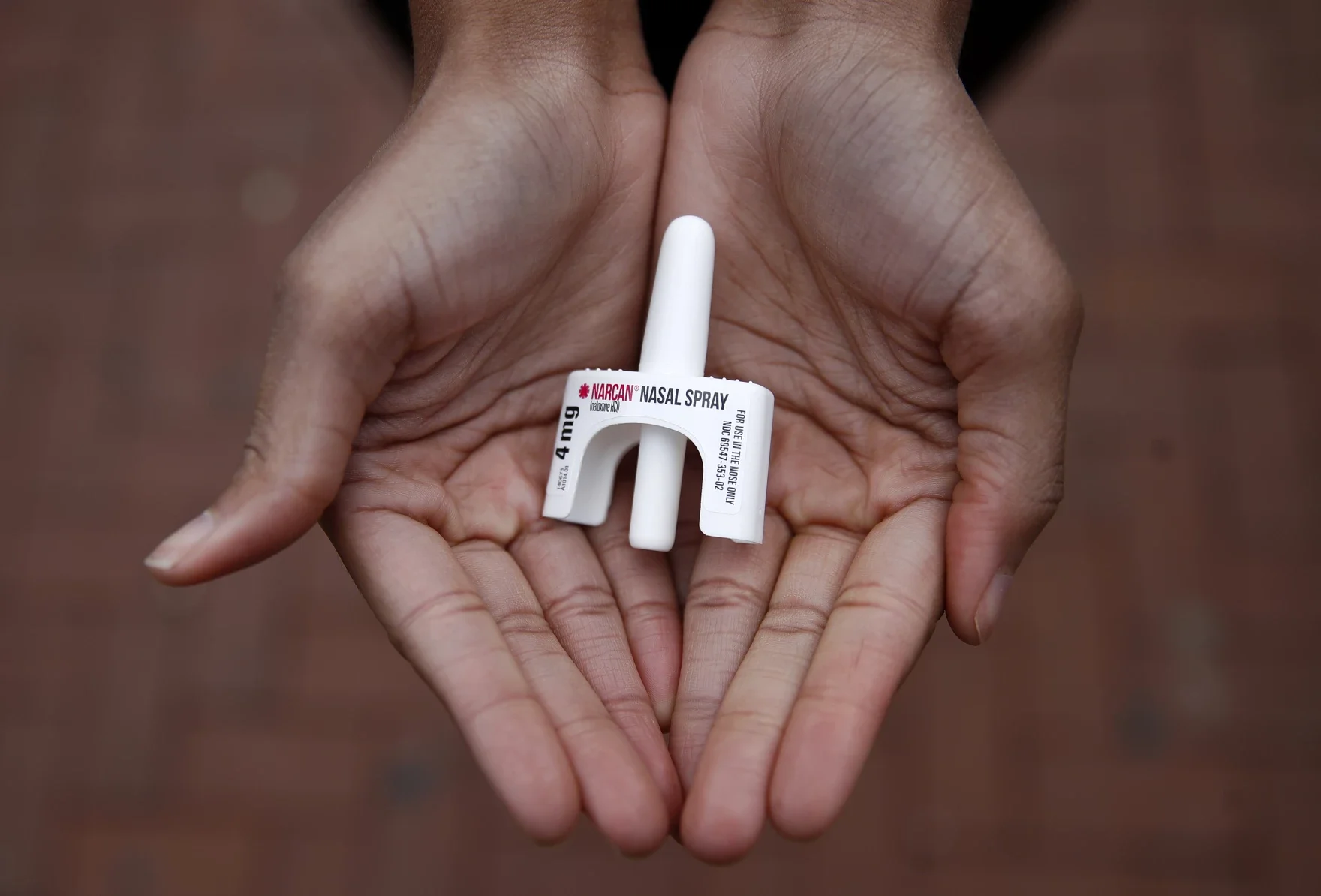 A person's hand holding a small plastic nasal spray bottle designed to look like a prescription medication bottle, with the label reading 'NARCAN NASAL SPRAY 4 mg'.