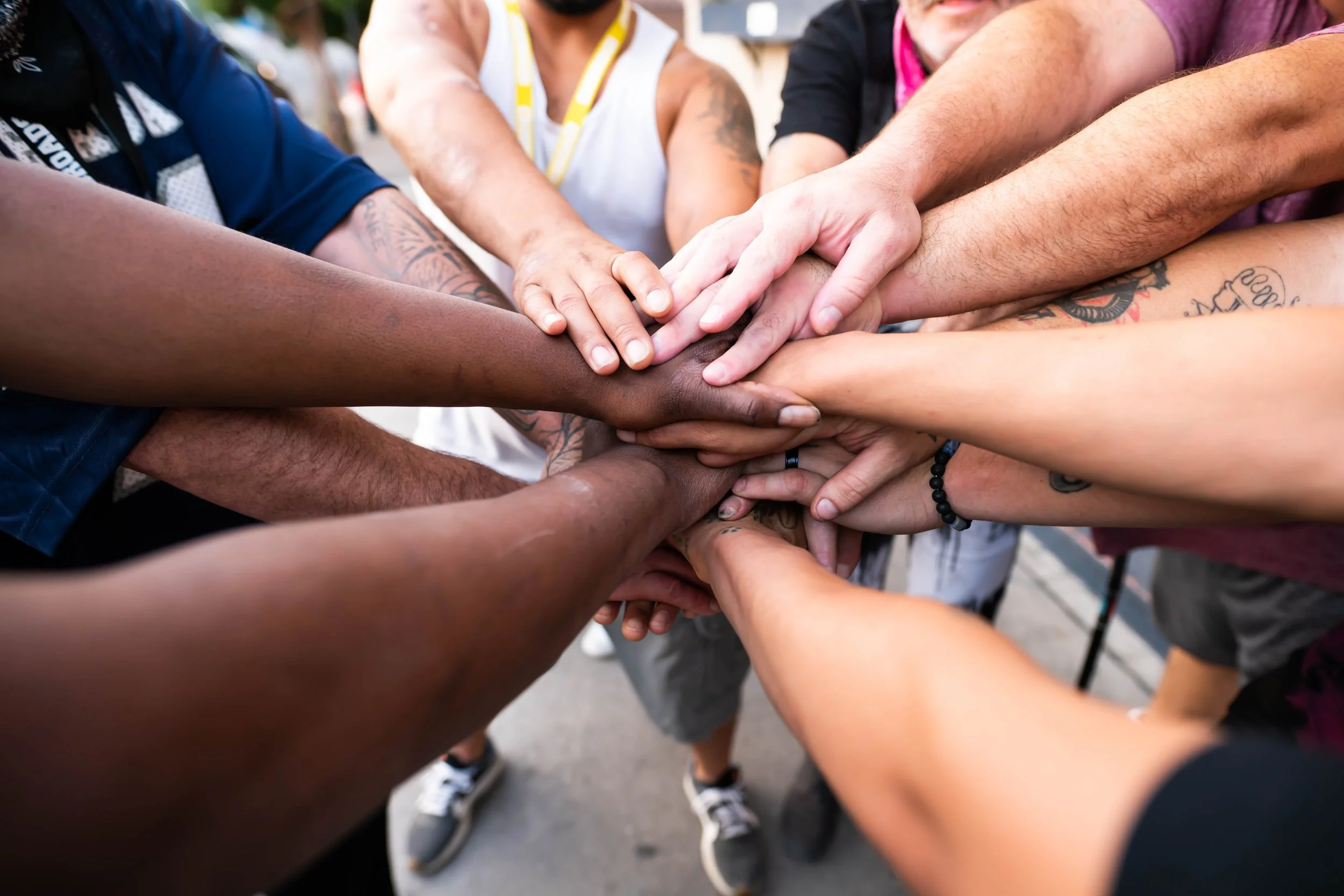 Multiple people of diverse backgrounds placing their hands together in a collective gesture of unity