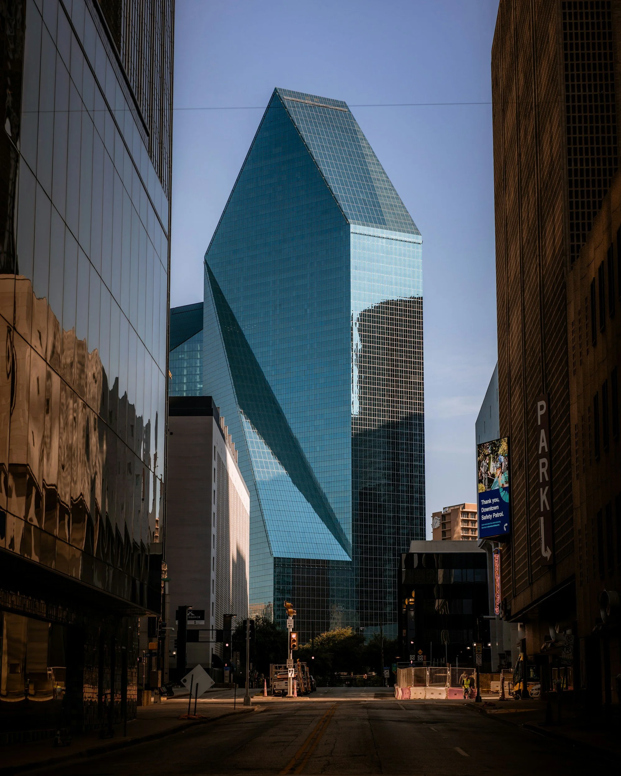 Tall modern glass skyscraper in downtown urban area with surrounding buildings and empty street.