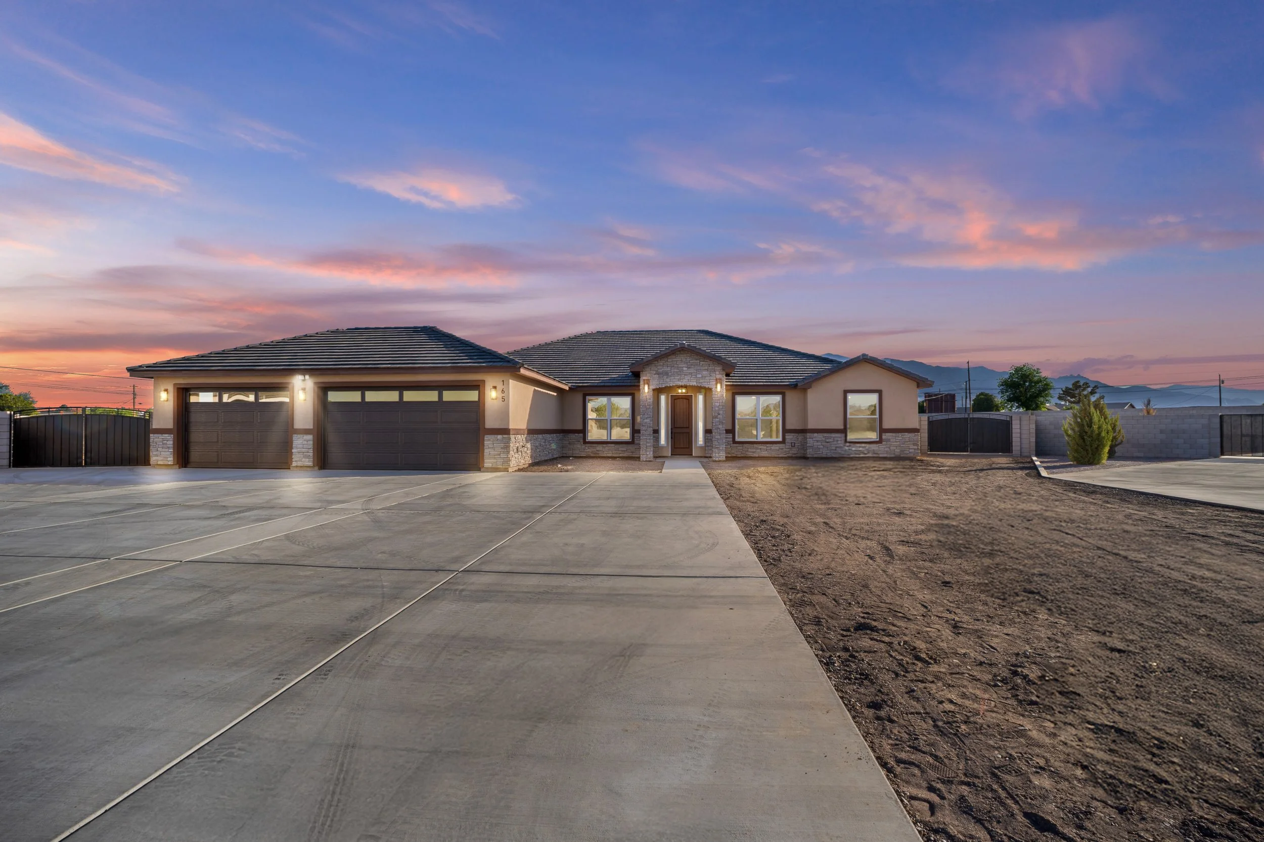 New single-story house with three garage doors, stone accents, front steps, and a concrete driveway at sunset.