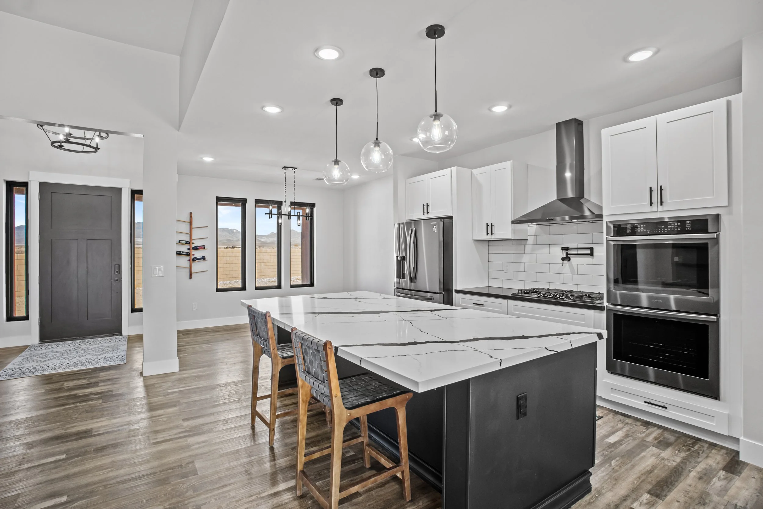 Modern kitchen with white cabinets, stainless steel appliances, a large island with a marble top, and wooden bar stools.