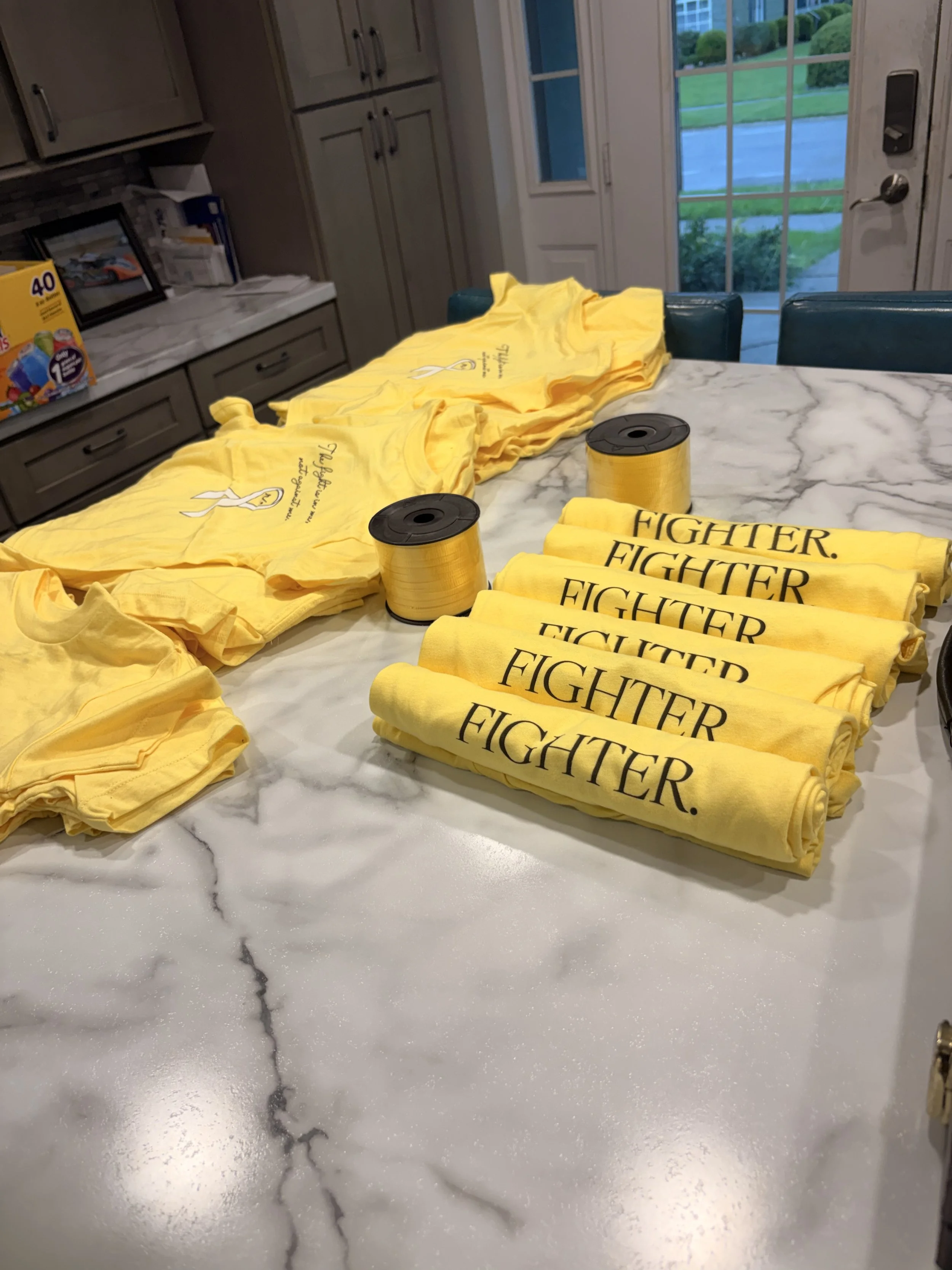 Yellow FIGHTER. shirts rolled and ready to be tied with yellow ribbon for the tote bags.